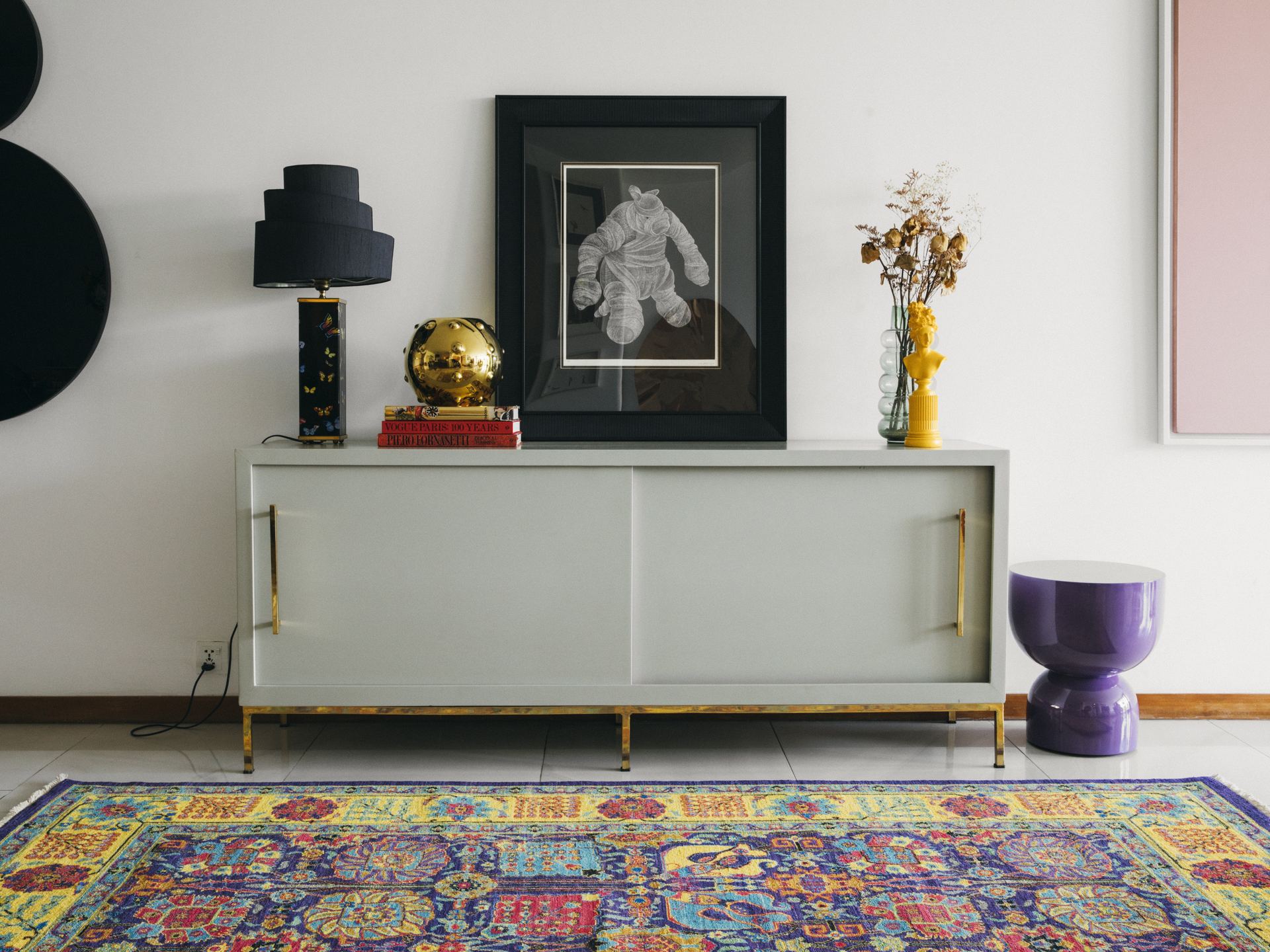 Grey lacquer sideboard styled with a framed illustration and a brass lamp on a floral Persian rug