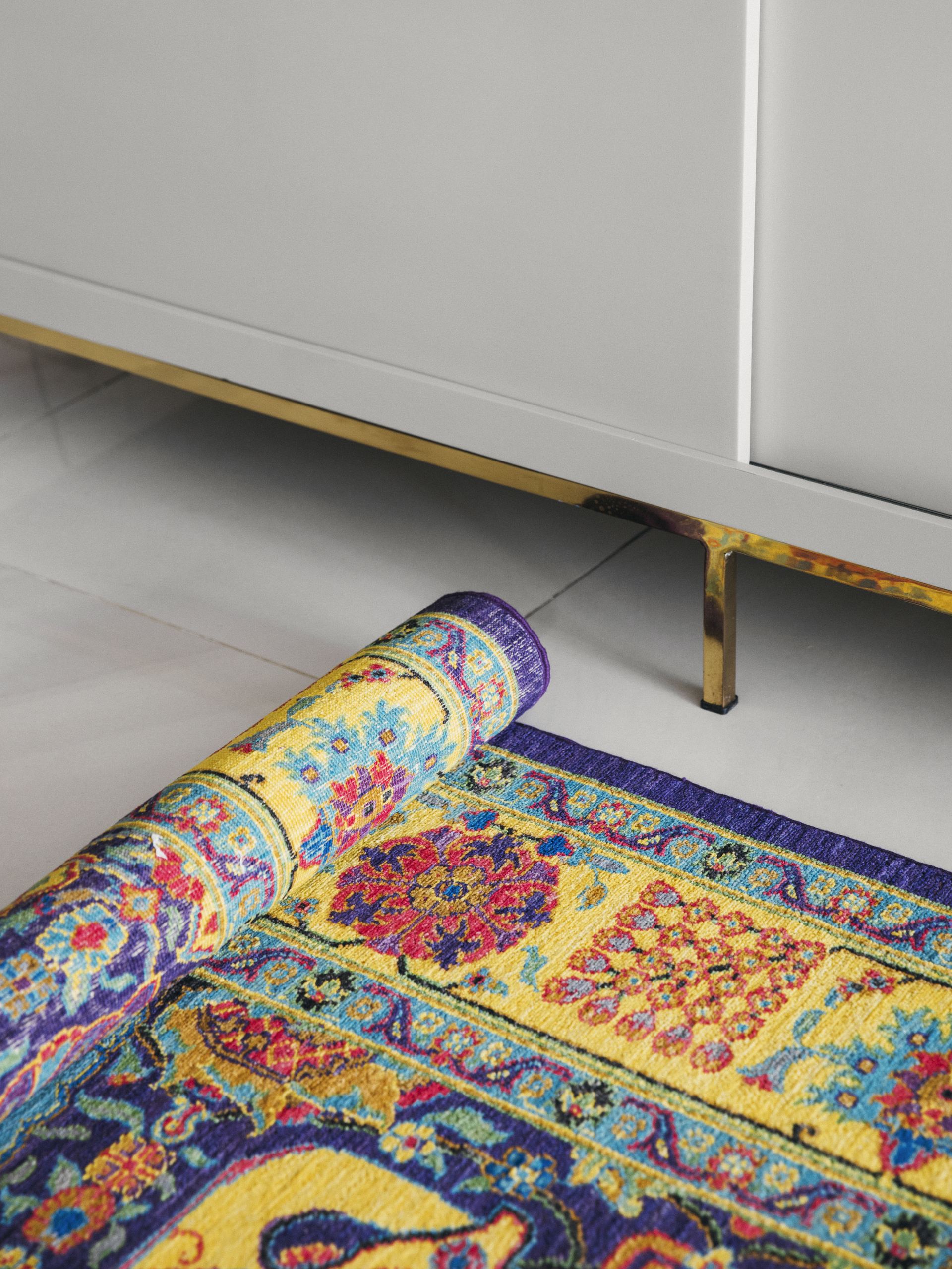Detail of a hand-knotted rug with a rolled corner beside a brass-legged sideboard