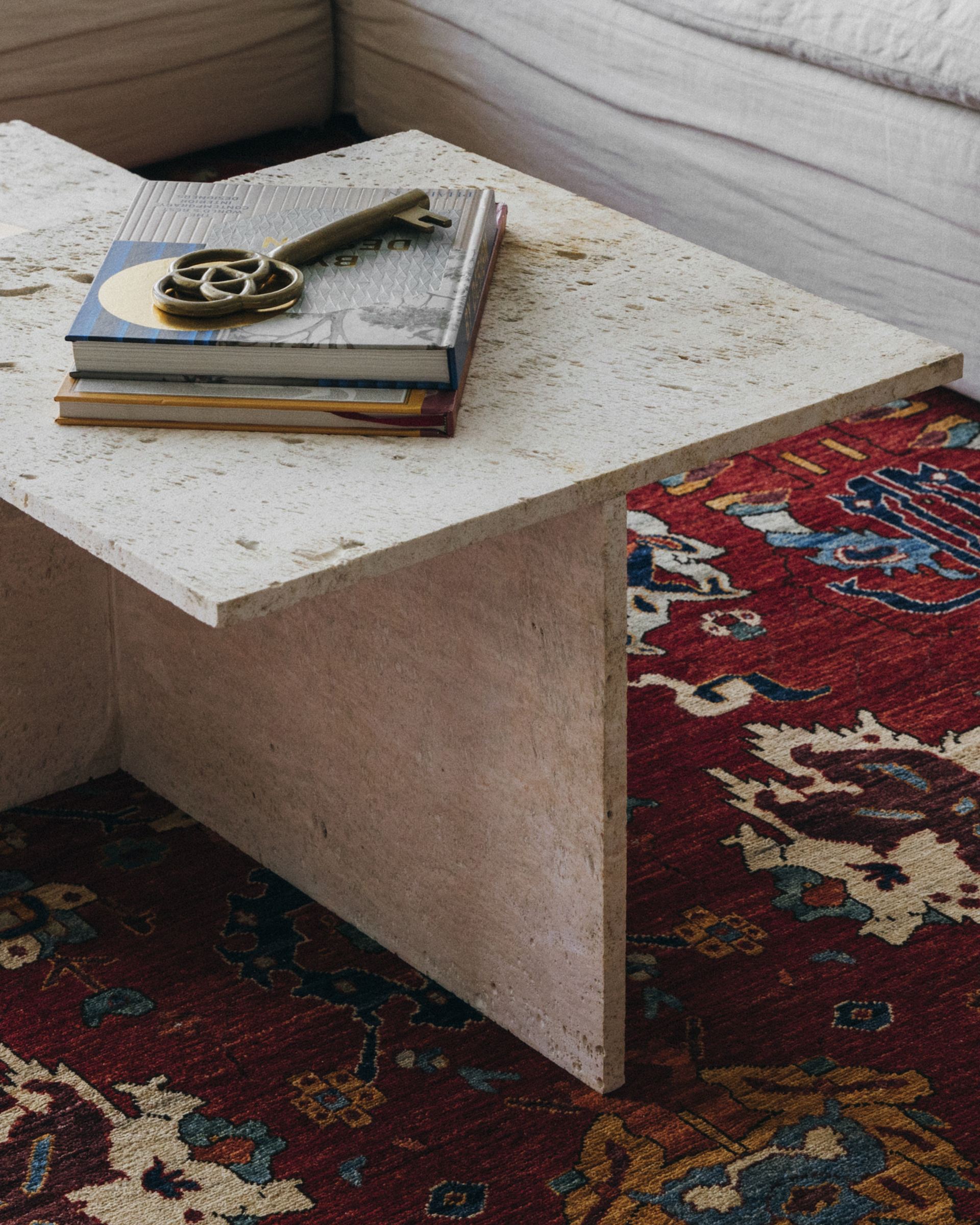 Travertine coffee table with a stack of books and a brass key ornament on a red Persian rug