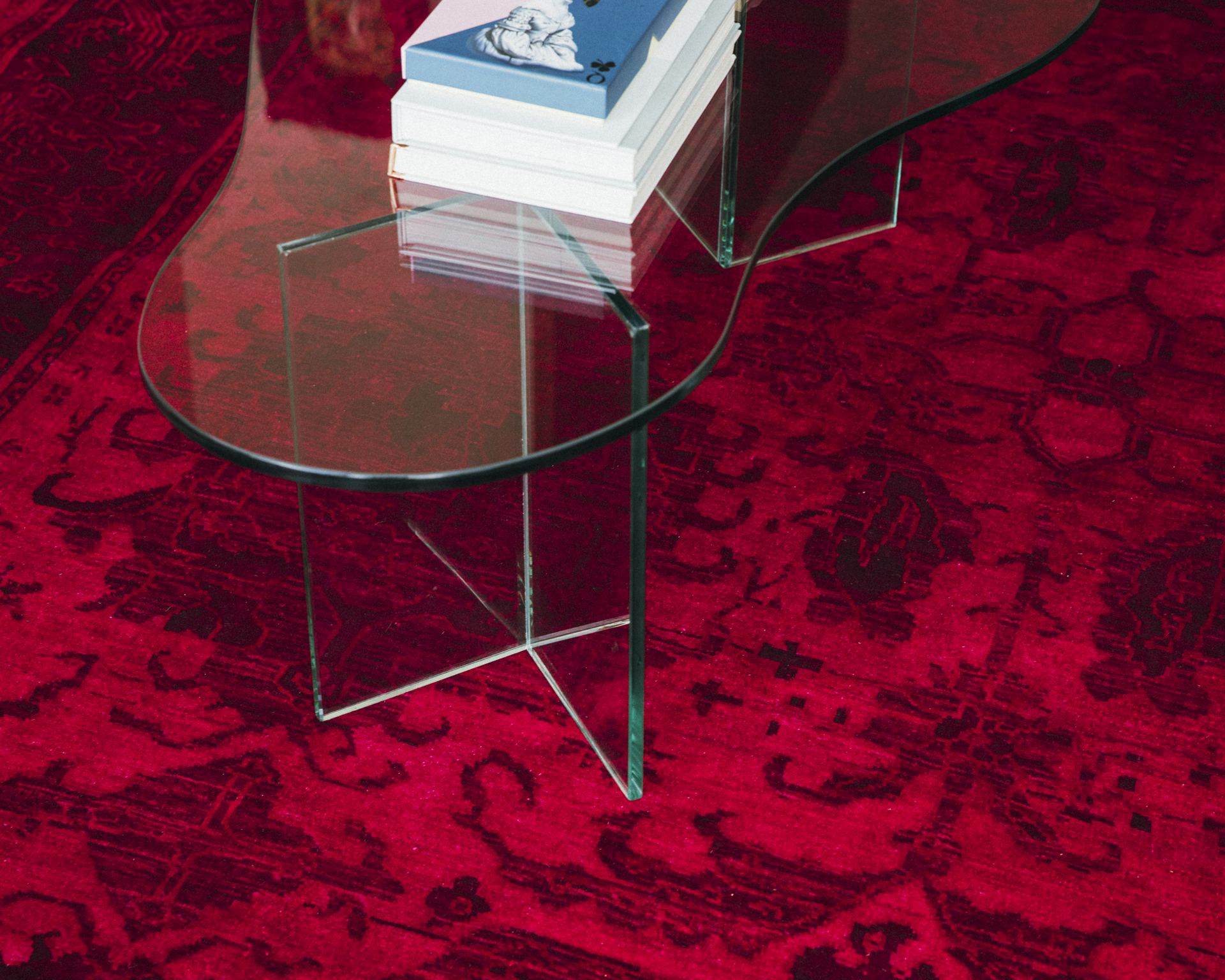 Glass coffee tables stacked with books on a burgundy Persian rug