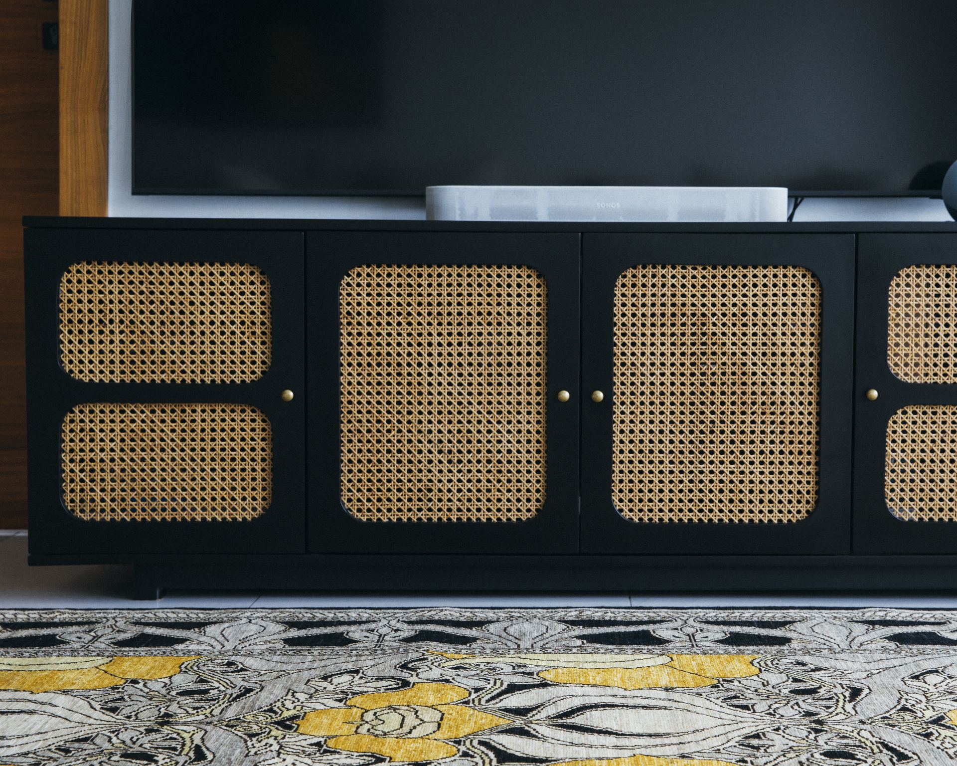 Detail of a black rattan-front media console on a floral Persian rug