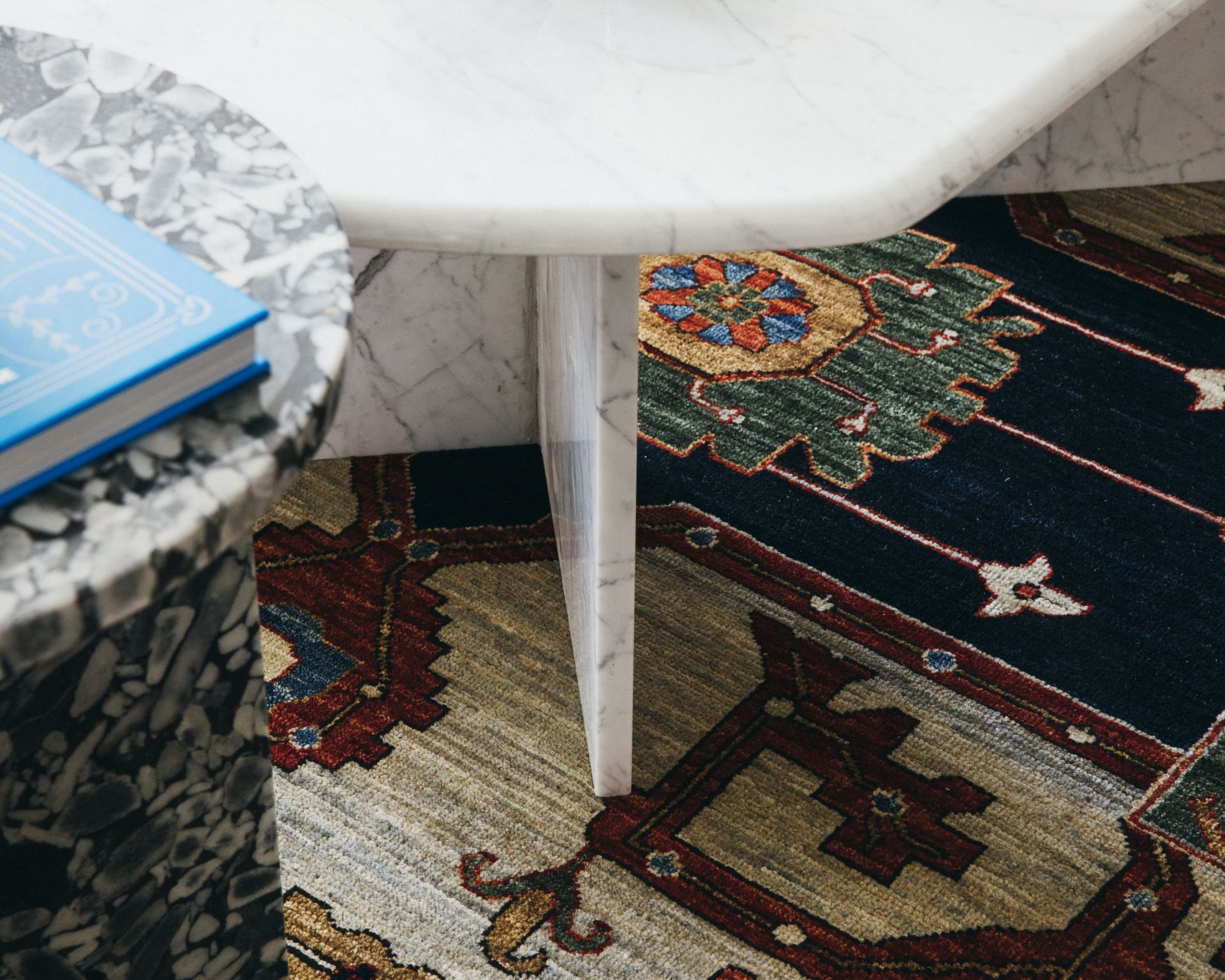 Detail of a marble side table leg beside a floral medallion Persian rug