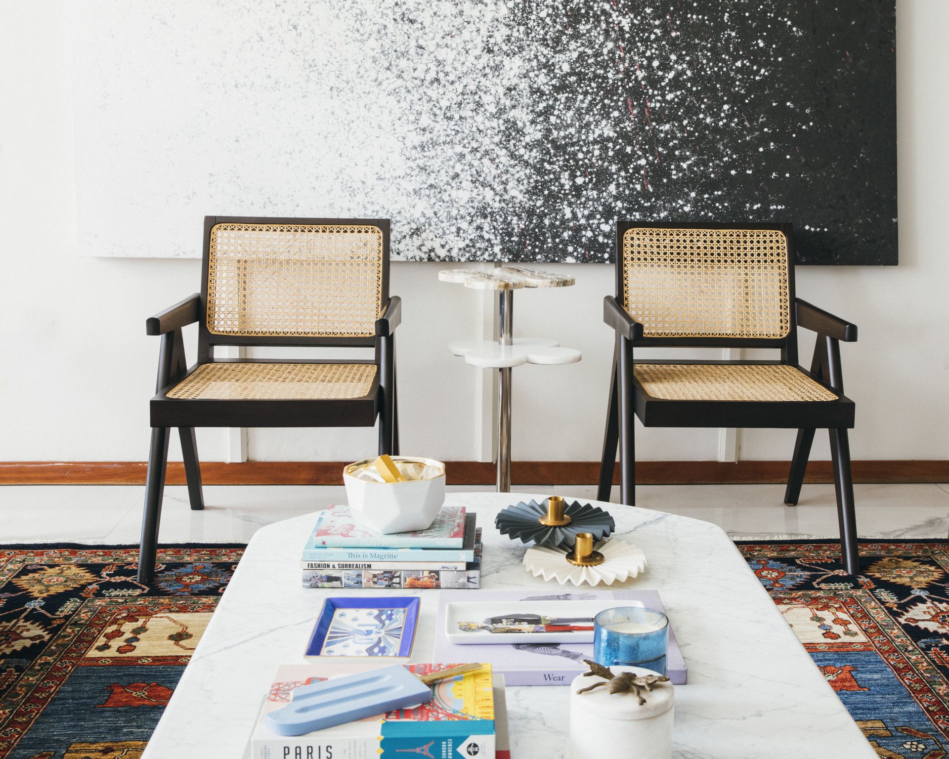 Cane armchairs beside a marble coffee table styled with books, set on a Persian rug