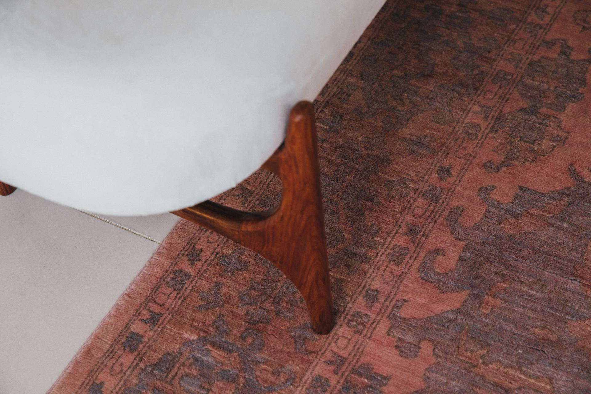 Detail of a wood chair leg beside a rust-toned Persian rug border