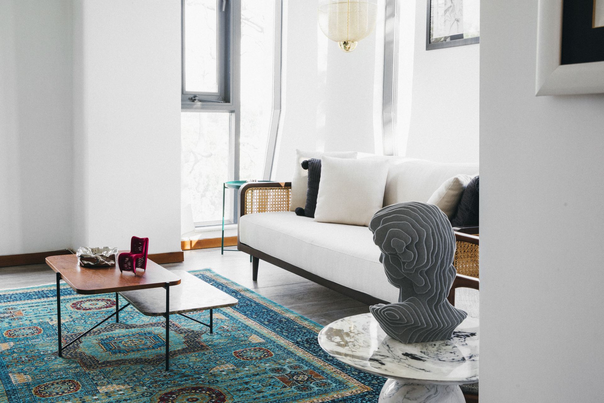 White bouclé sofa beside a sculptural bust and marble side table on a teal Persian rug