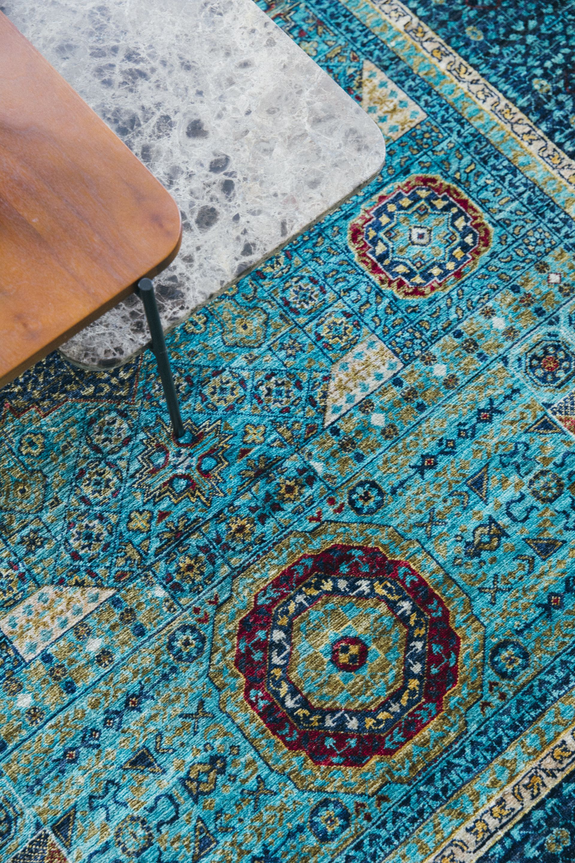 Detail of a wood coffee table leg on a teal medallion Persian rug