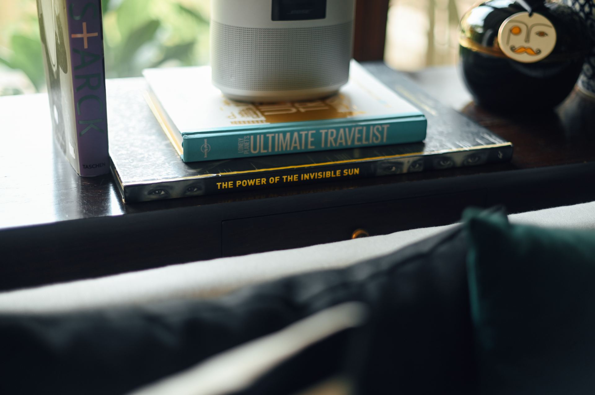 Hardcover books beside a bedside lamp on a dark console