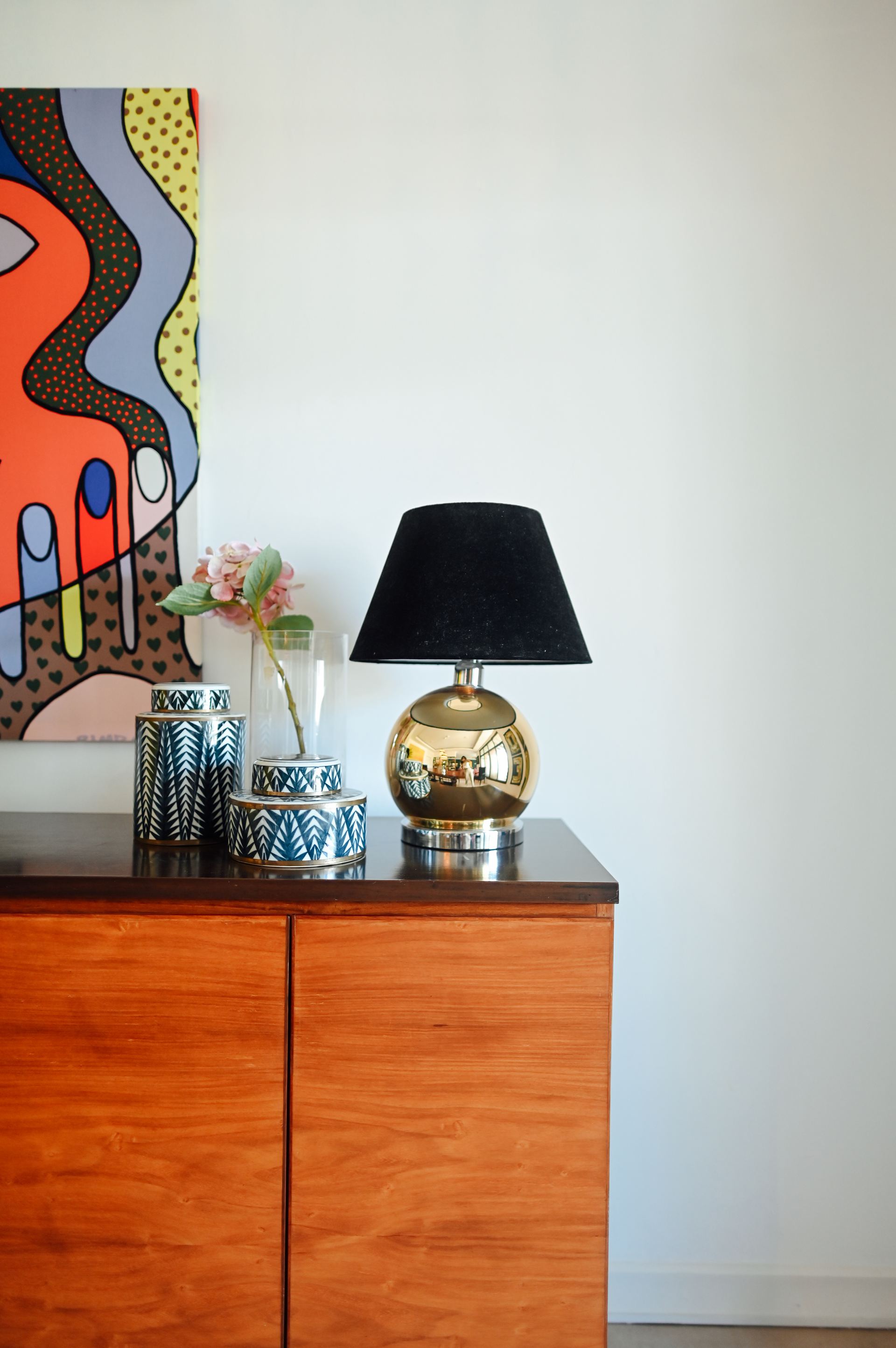 Pop-art painting above a walnut sideboard styled with a brass lamp