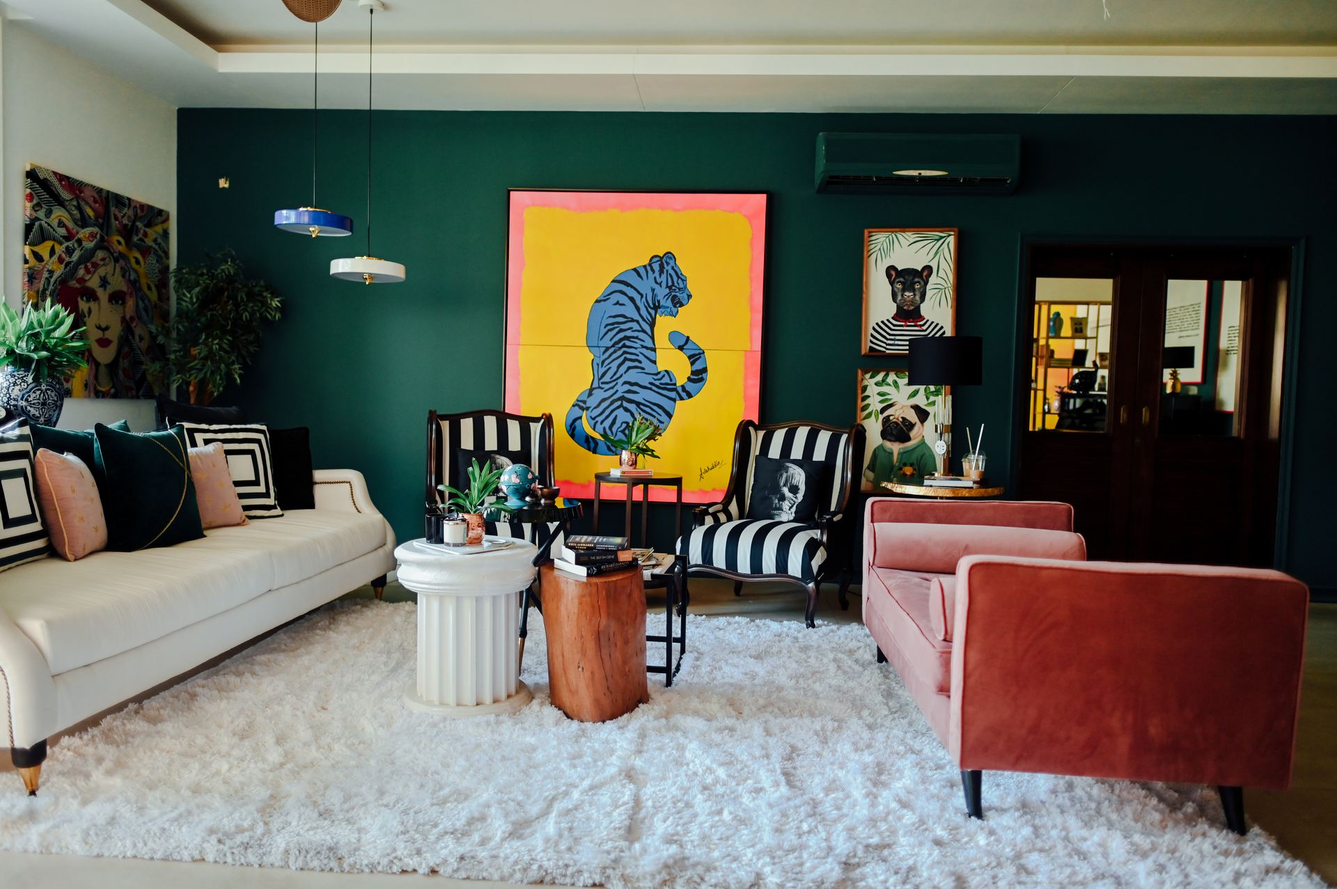 Wide view of the forest-green living room with striped armchairs and a blush sofa