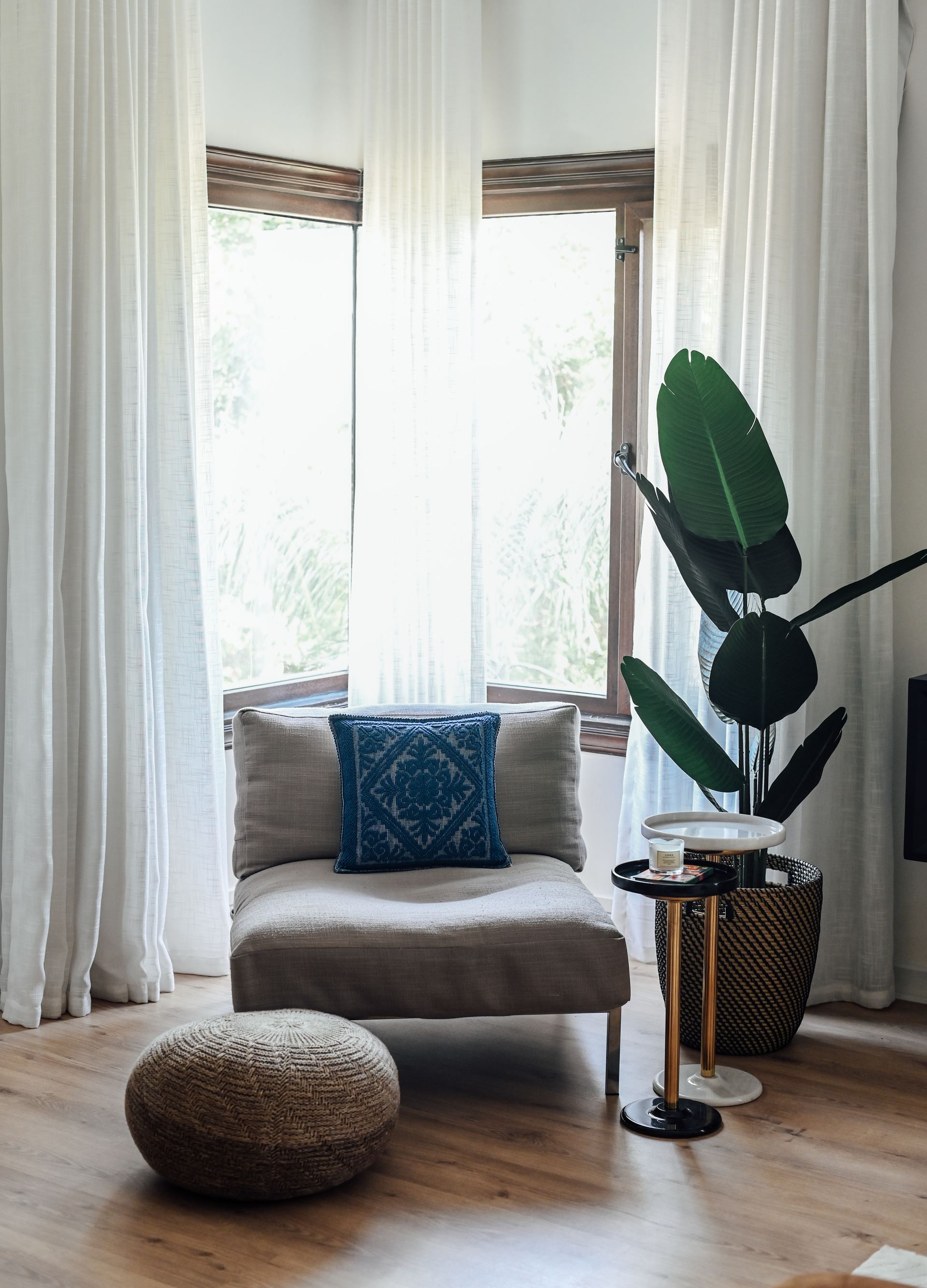 Reading nook with a linen armchair and embroidered cushion by a bay window