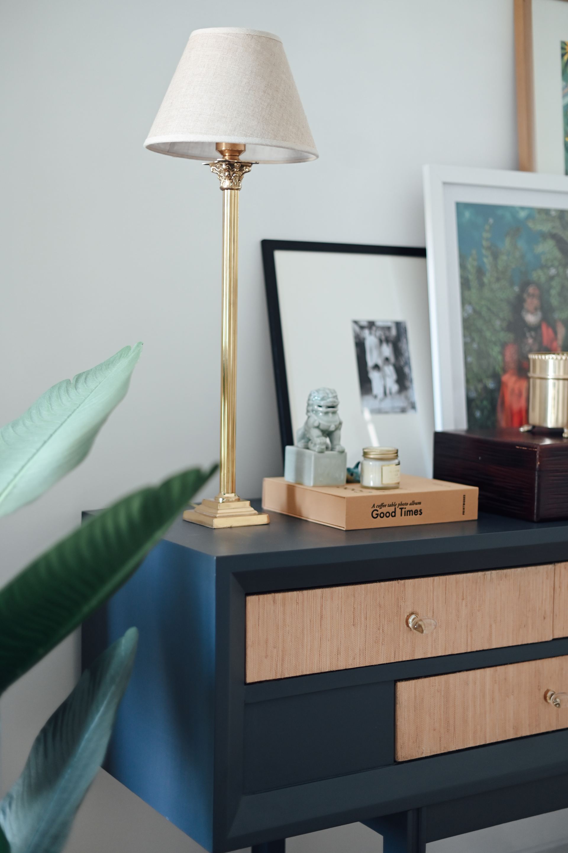 Brass table lamp beside framed art on a rattan-drawer console