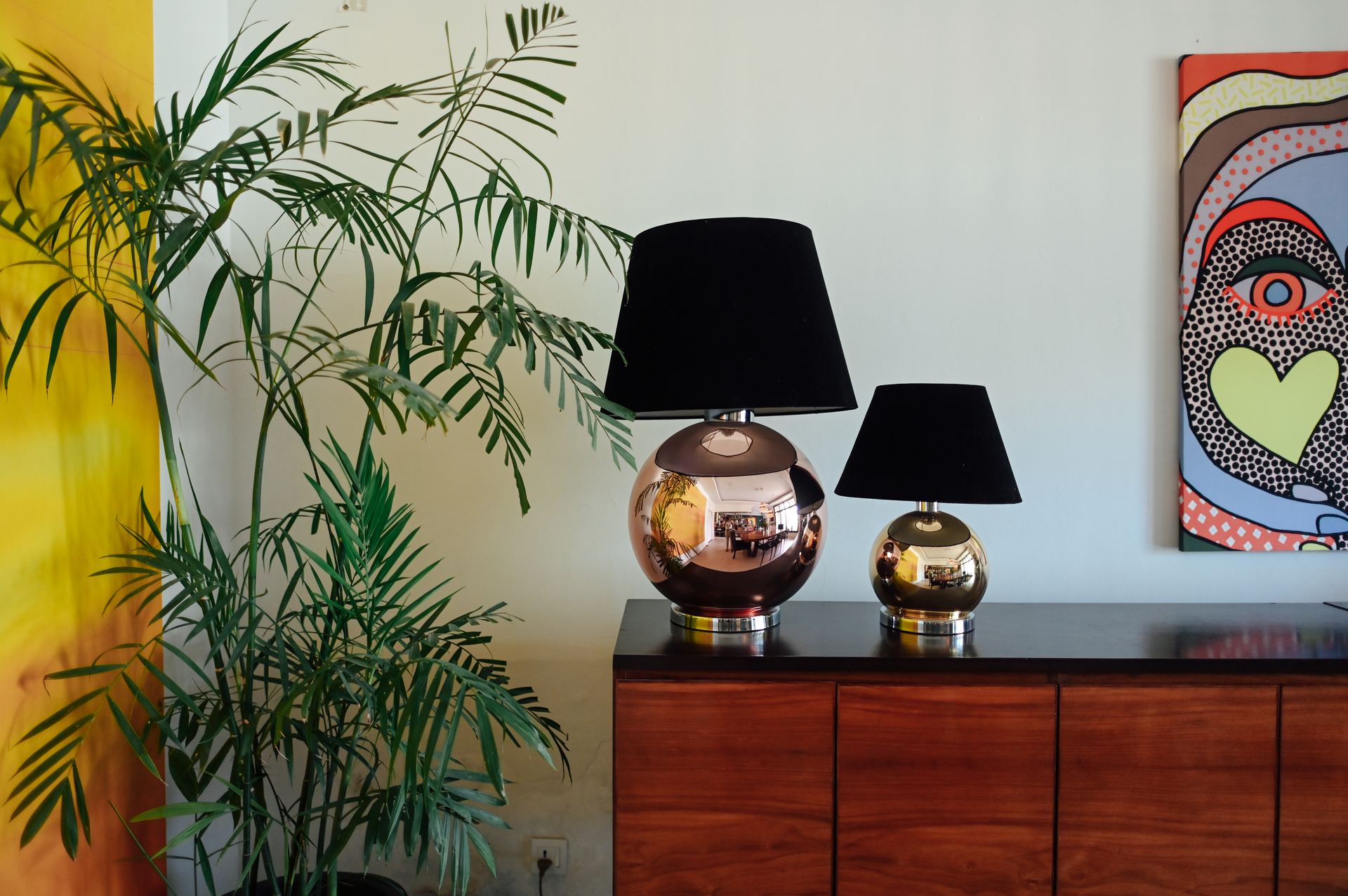 Pair of brass ball lamps with black shades on a walnut sideboard
