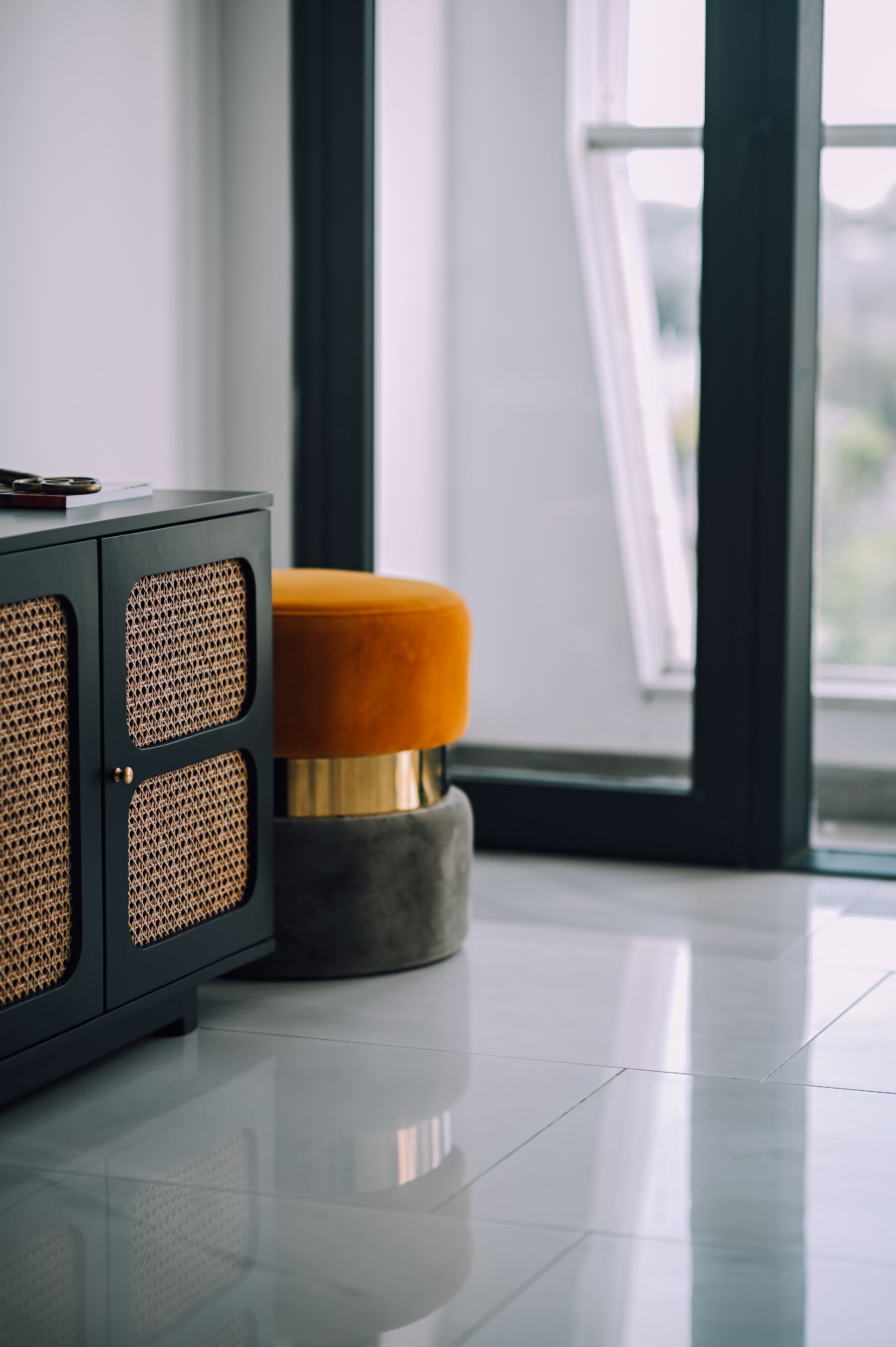 Rattan-front cabinet beside a mustard velvet stool by a window