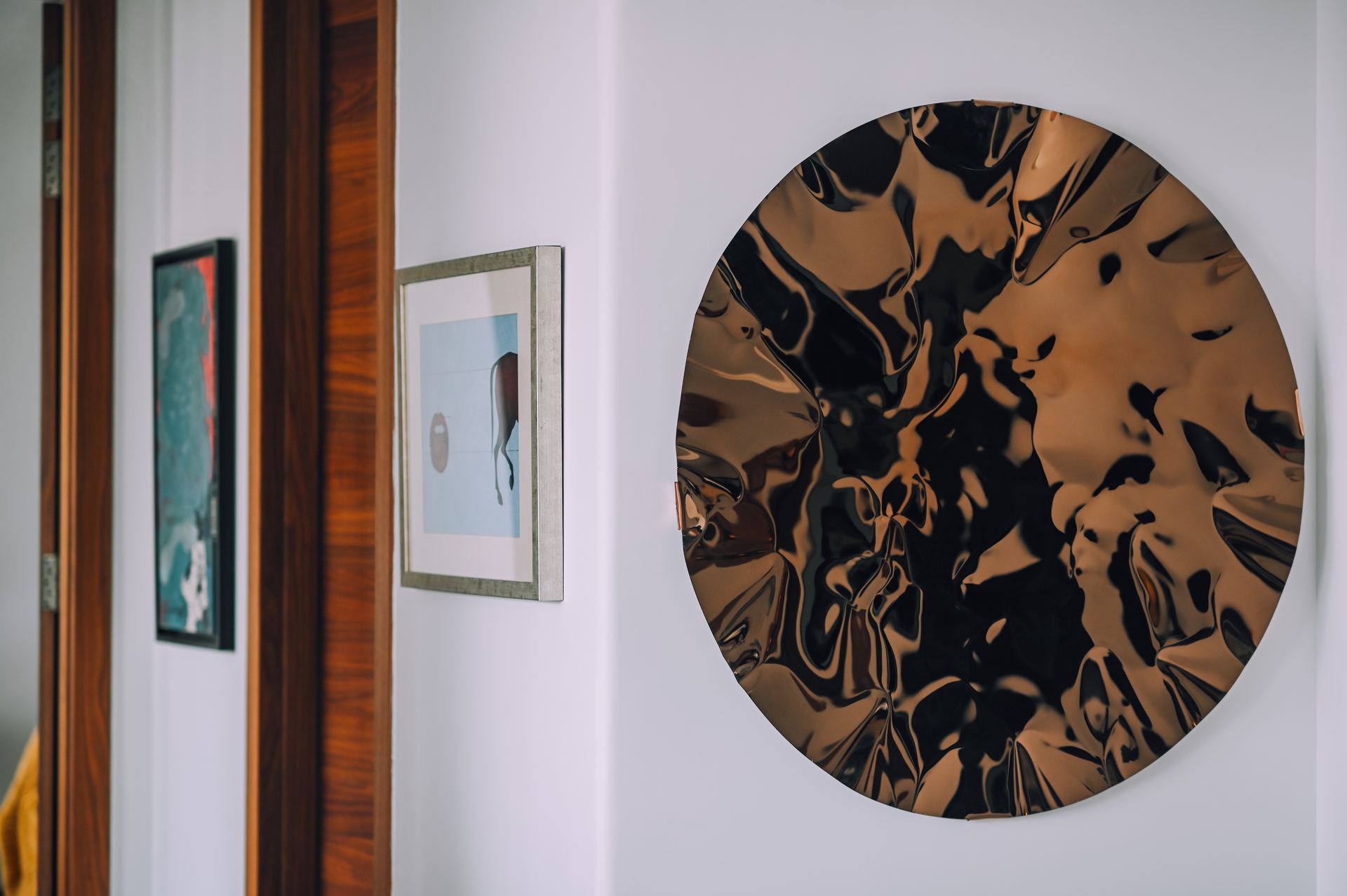Molten-bronze circular sculpture beside framed art in a hallway