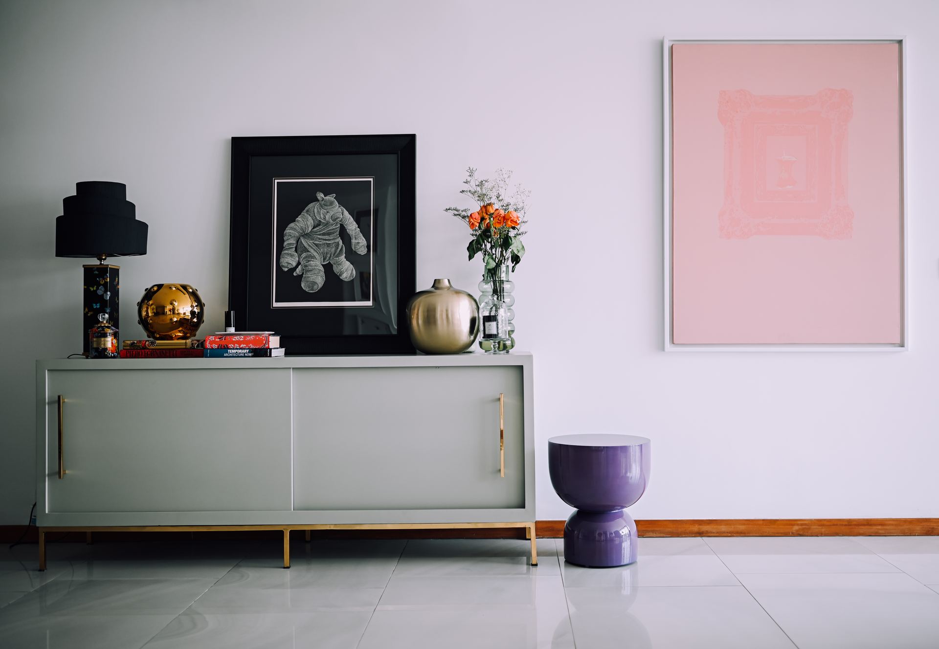 Grey sideboard styled with framed photos, a black lamp, and a soft pink canvas
