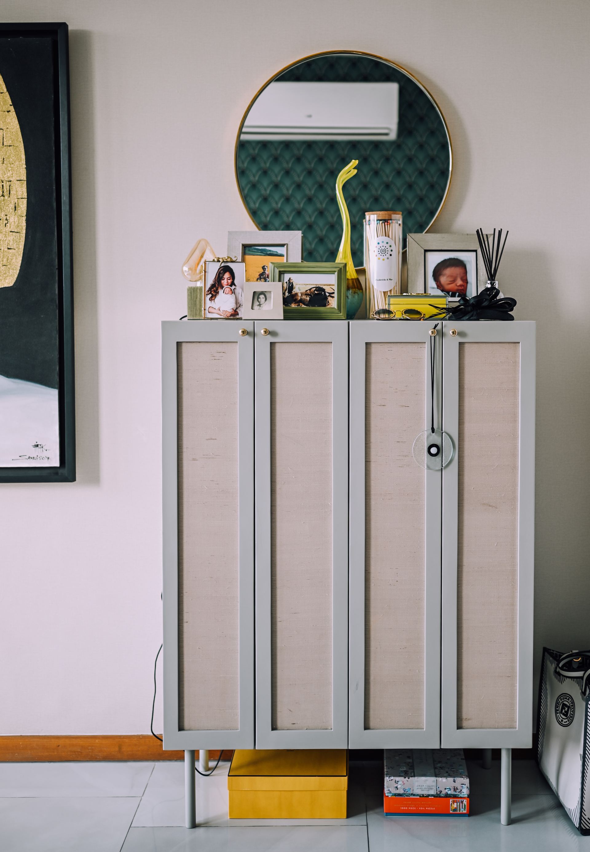 Grey cabinet topped with framed photos and a round mirror