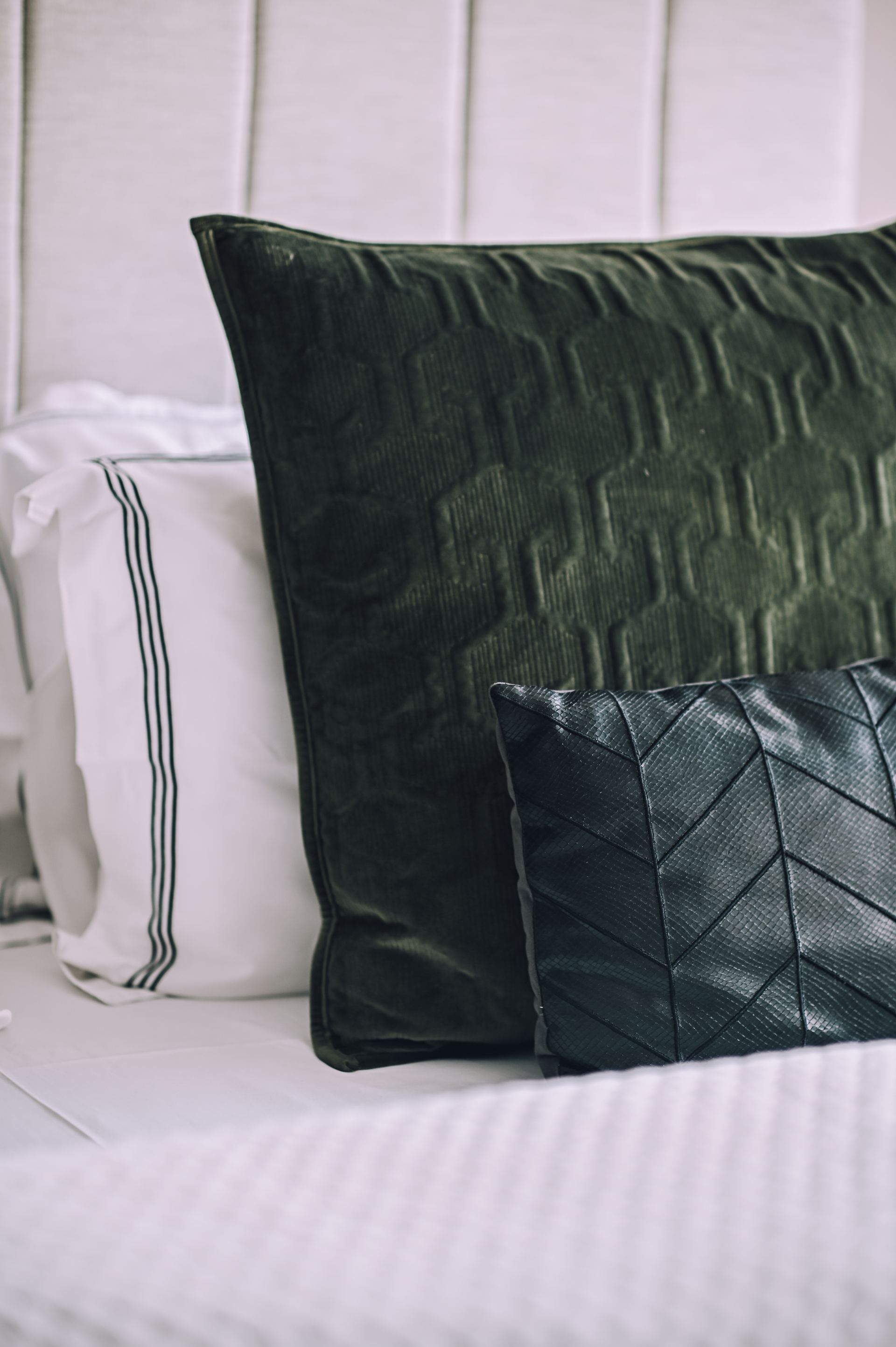 Dark quilted cushions stacked against a panelled headboard