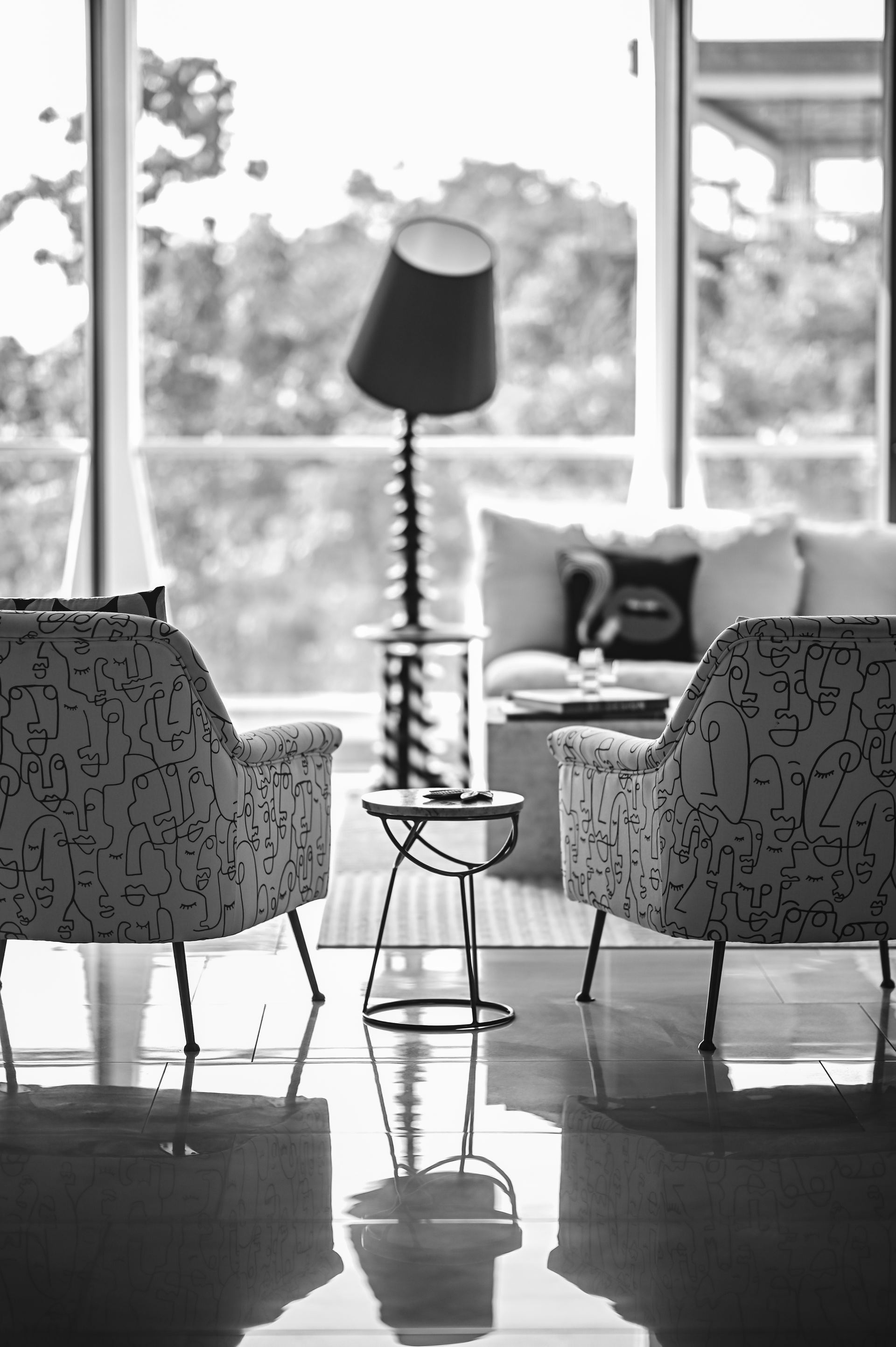 Black-and-white view of face-print armchairs beside a sculptural floor lamp