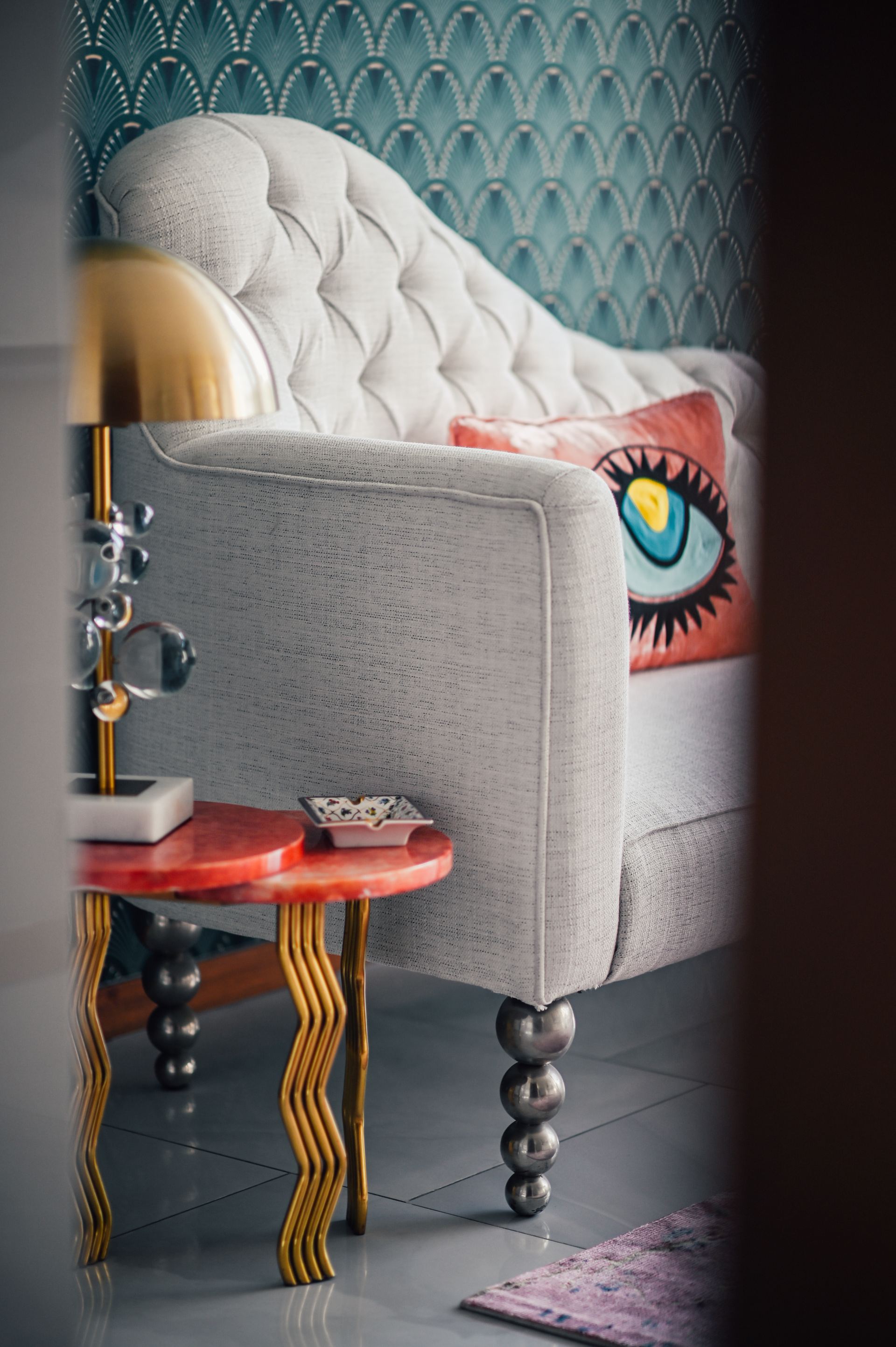 Tufted grey armchair with an embroidered eye cushion beside a coral marble side table