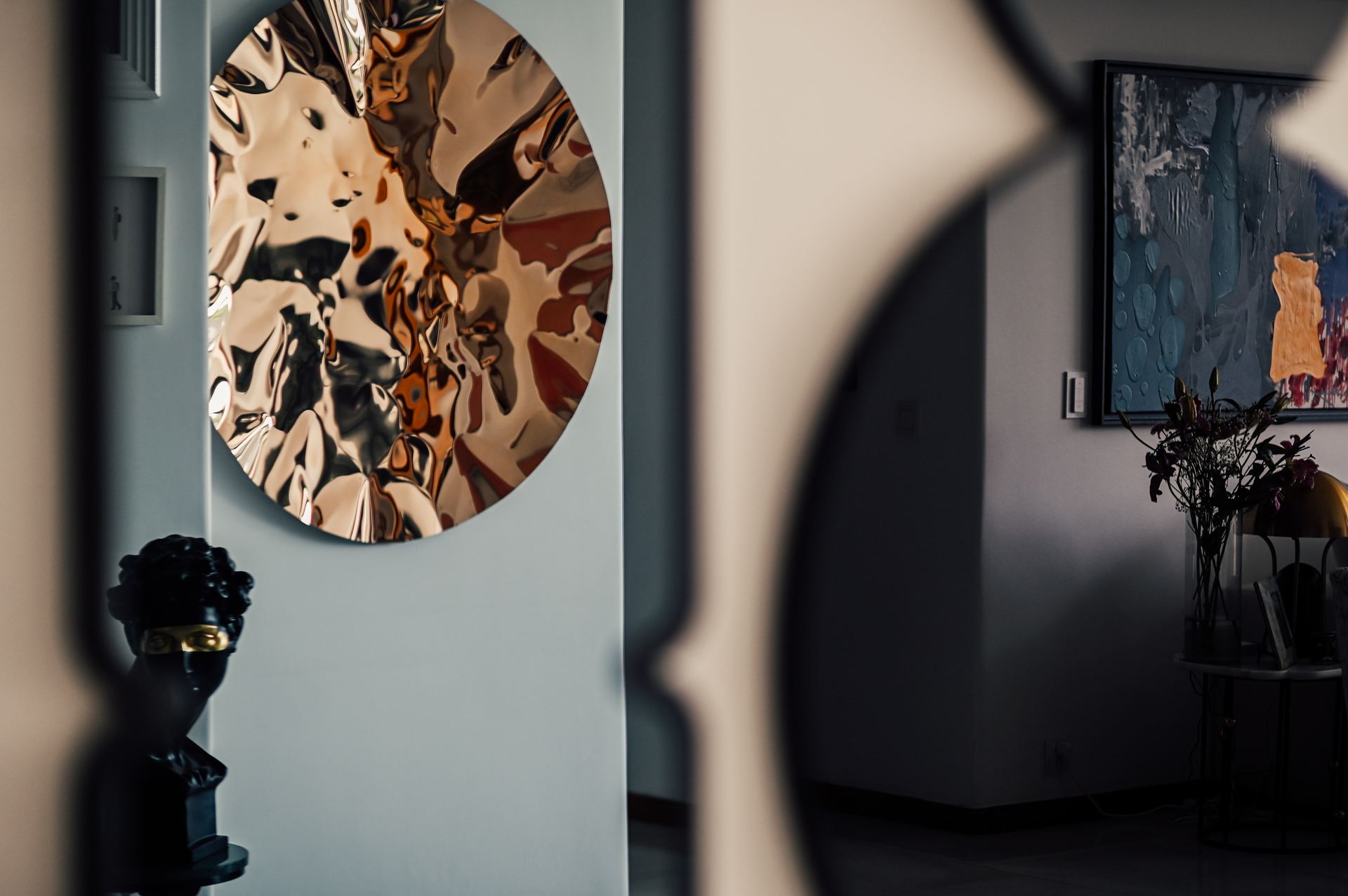 Molten bronze circular sculpture beside a framed abstract painting