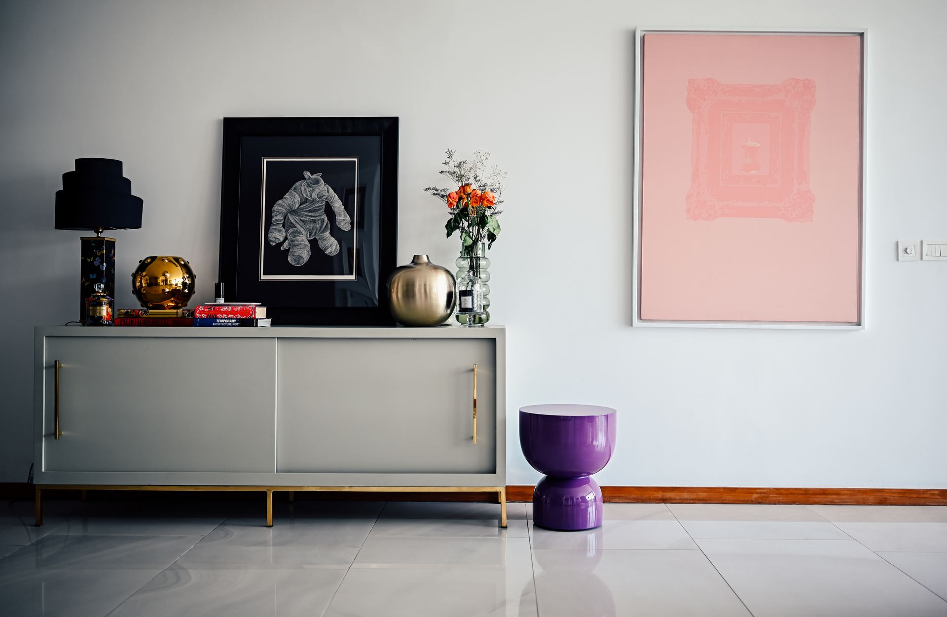 Grey sideboard styled with a framed illustration, brass ornaments, and a soft pink canvas