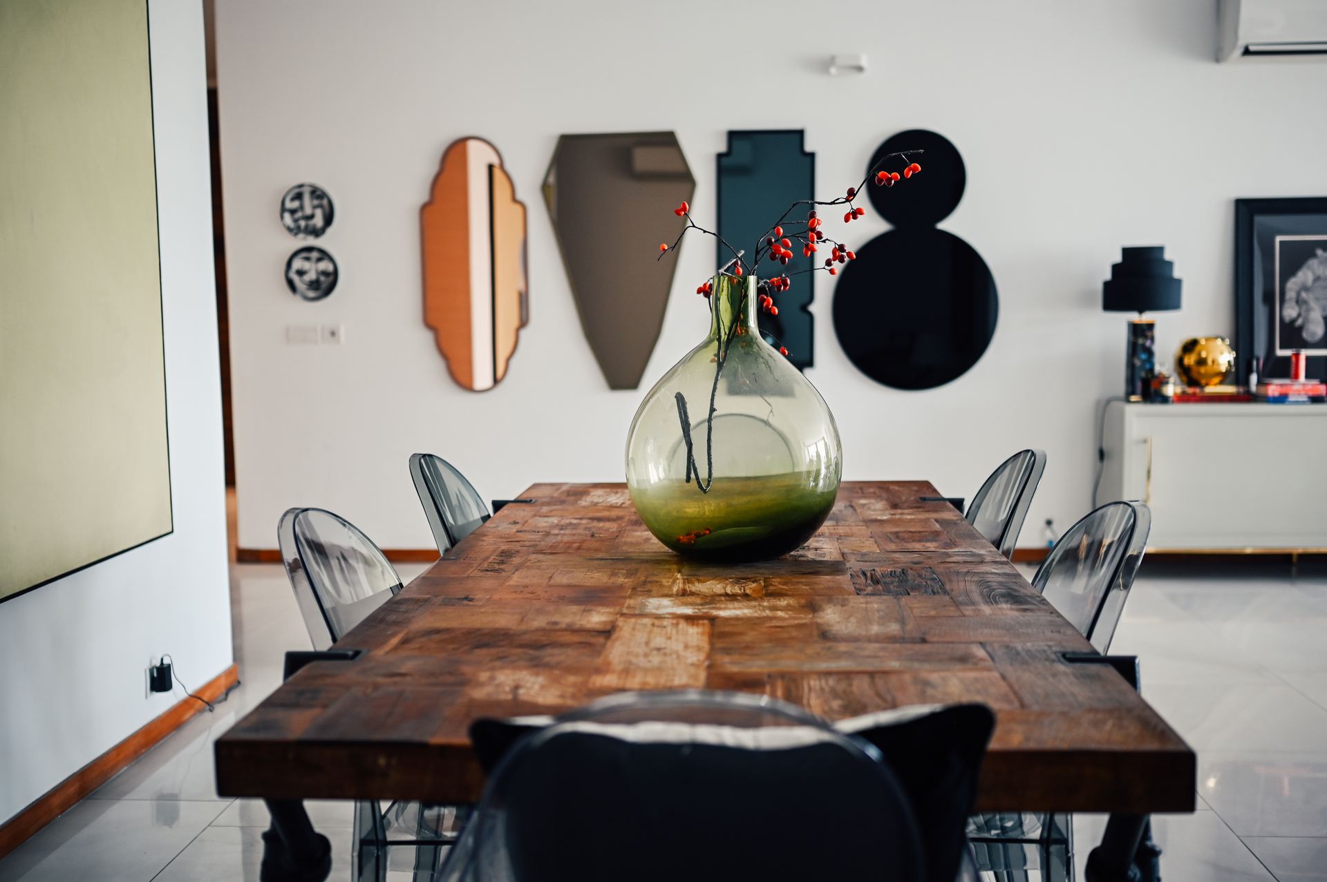 Reclaimed-wood dining table with an amber glass vase and art-deco wall decor