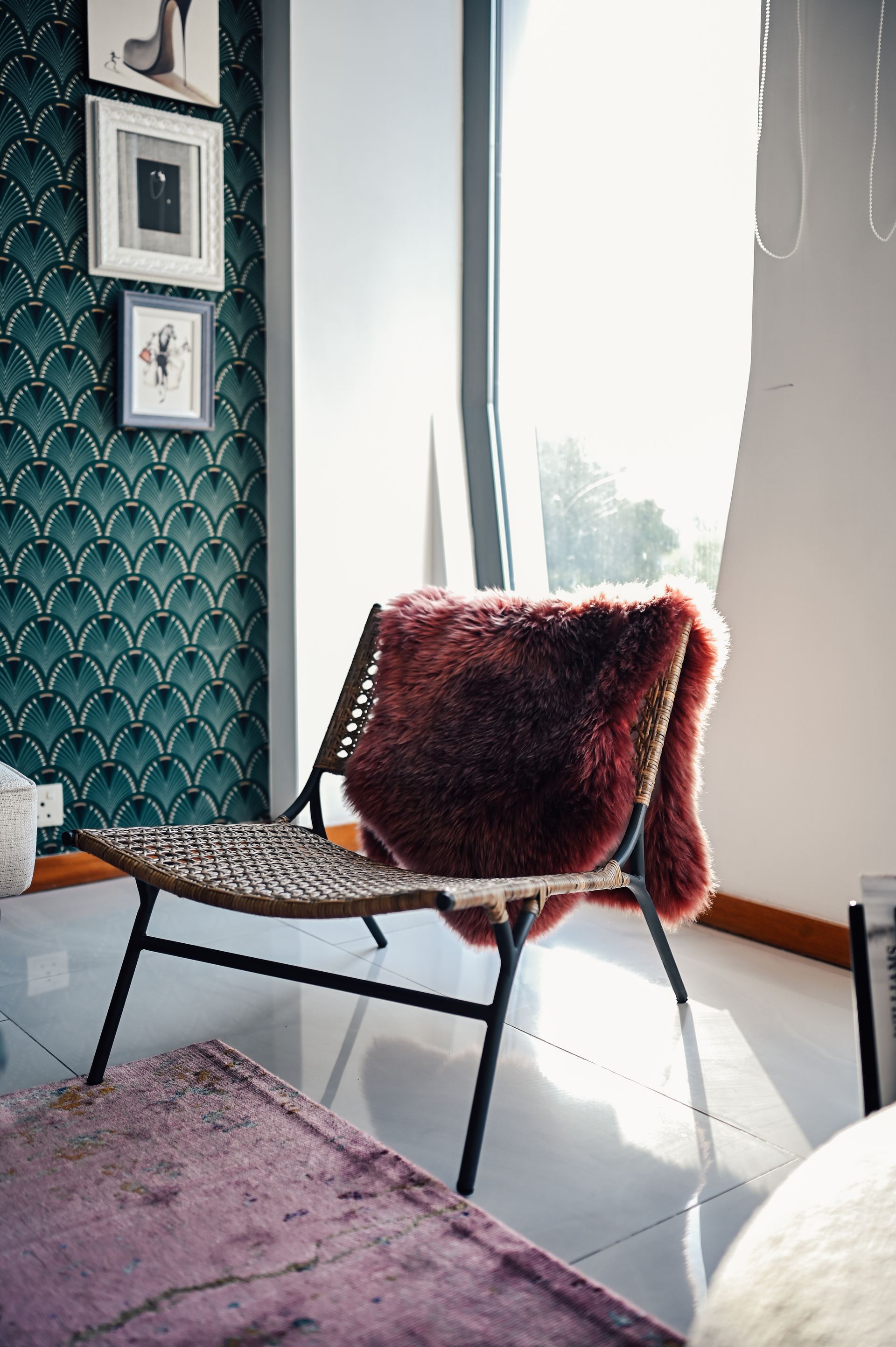 Wicker lounge chair draped with a burgundy sheepskin against teal scalloped wallpaper