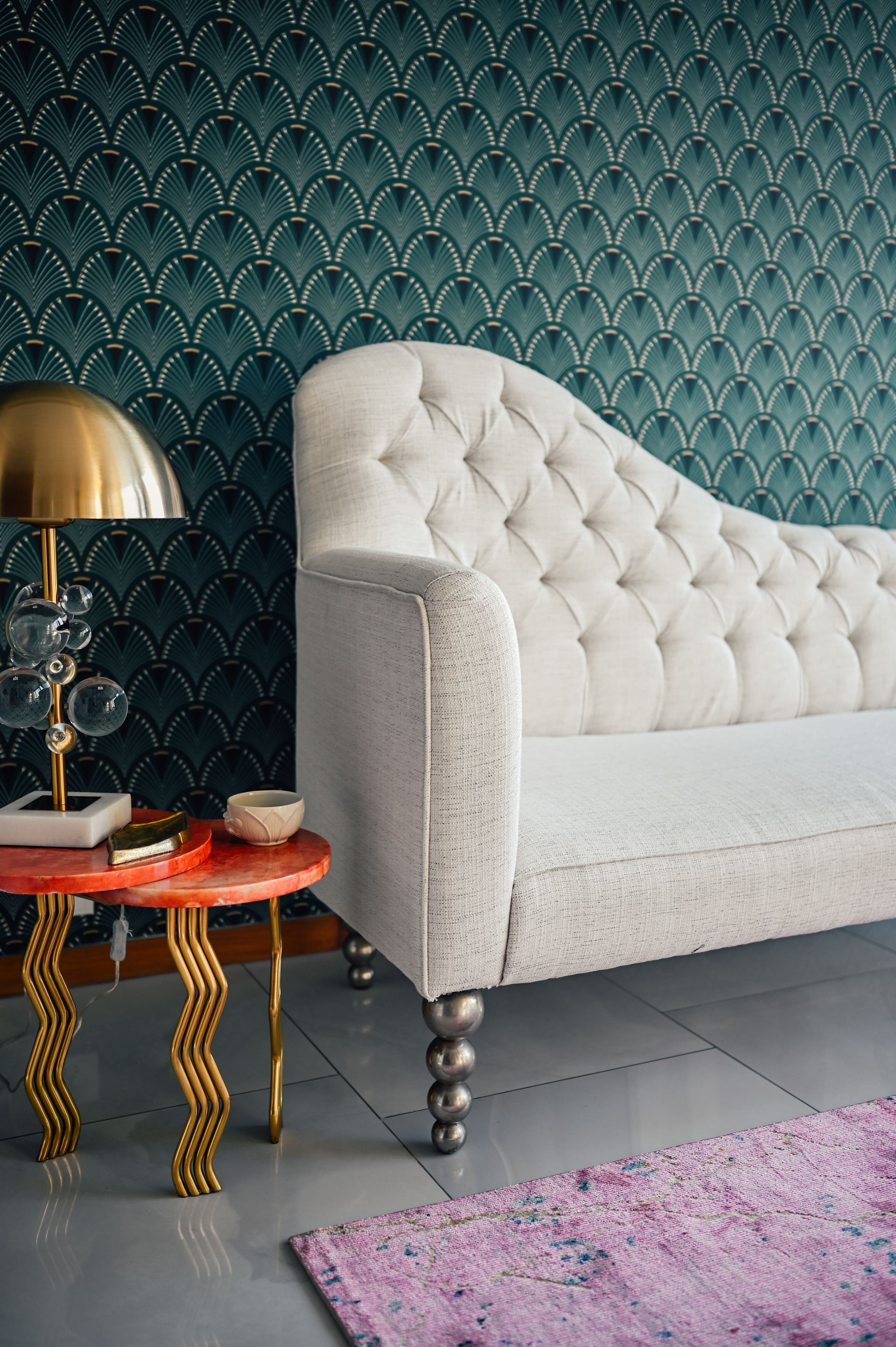 Tufted cream chaise beside a brass bubble lamp on a coral marble side table