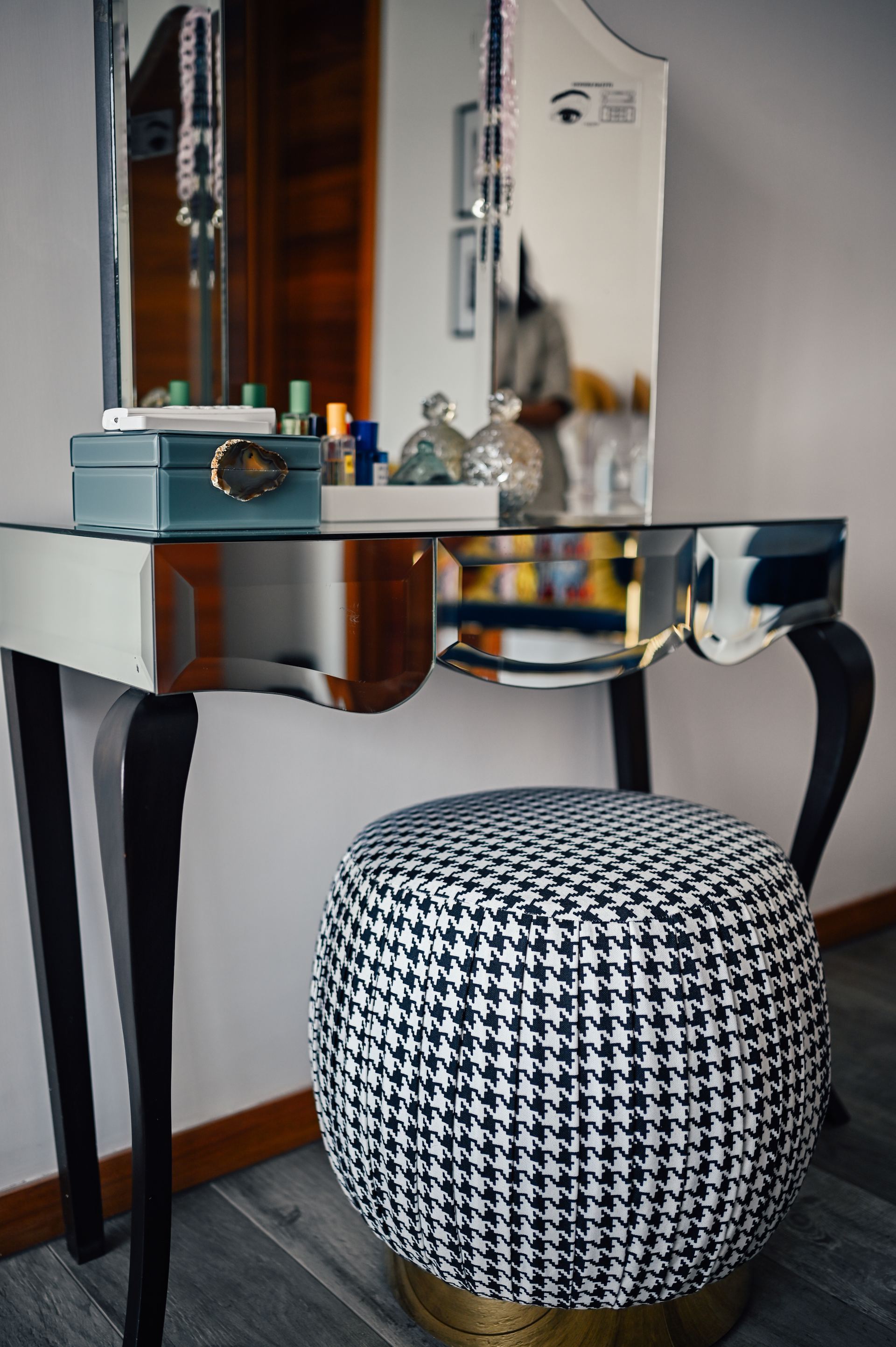Mirrored vanity table styled with perfume bottles and a houndstooth stool