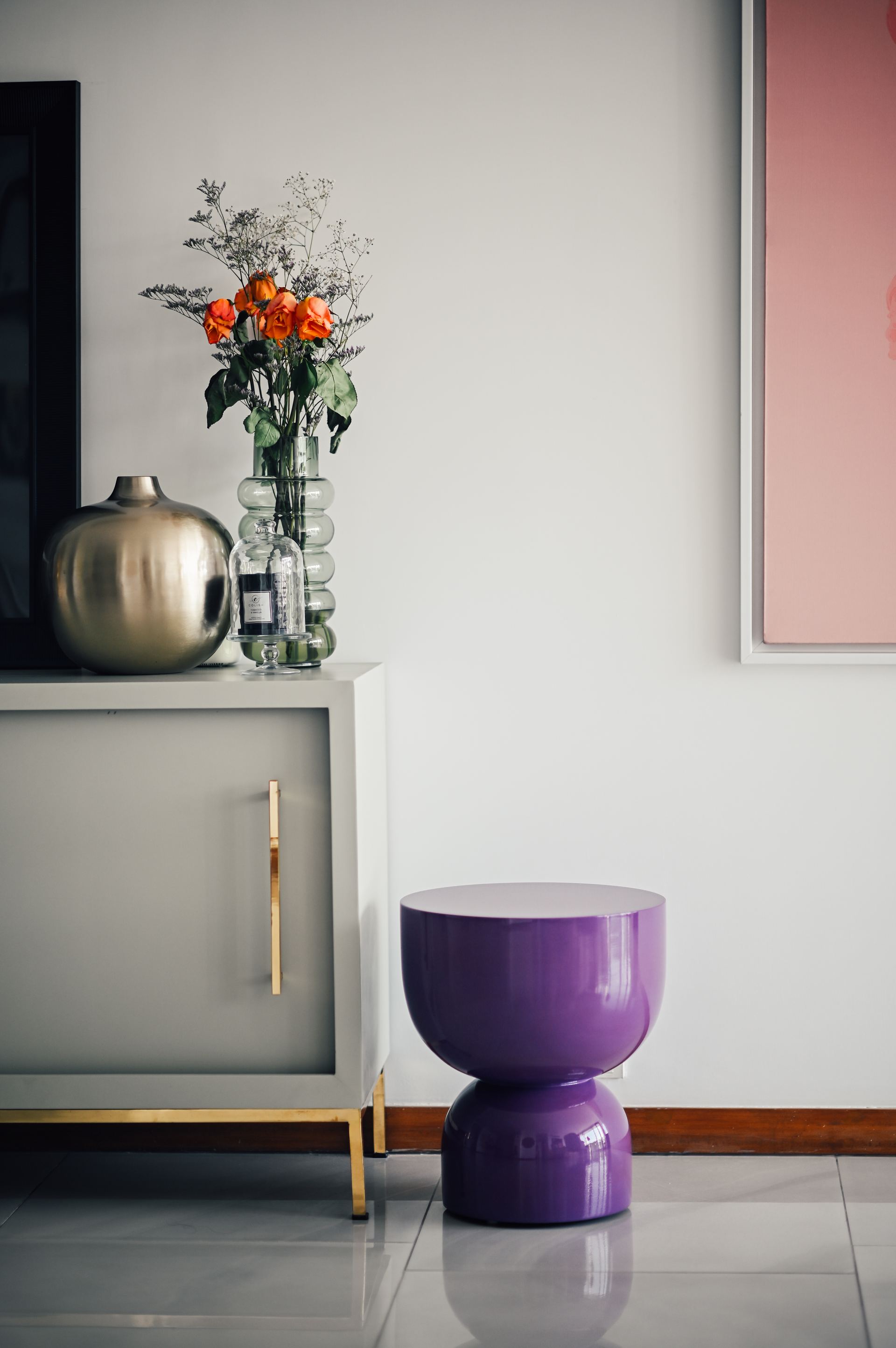 Grey sideboard styled with a brass vase of roses beside a purple hourglass stool