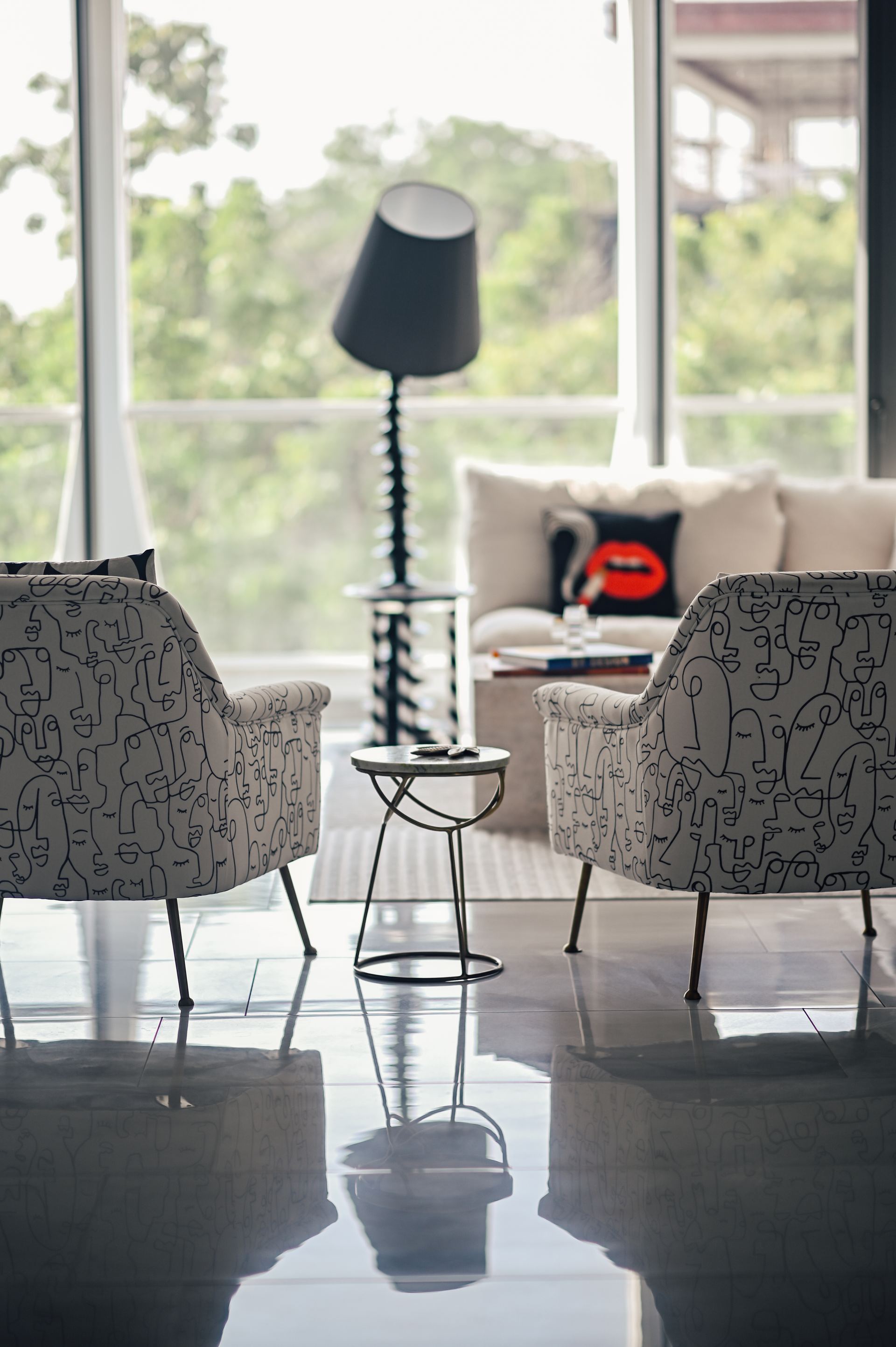 Face-print armchairs facing each other beside a ribbed black floor lamp