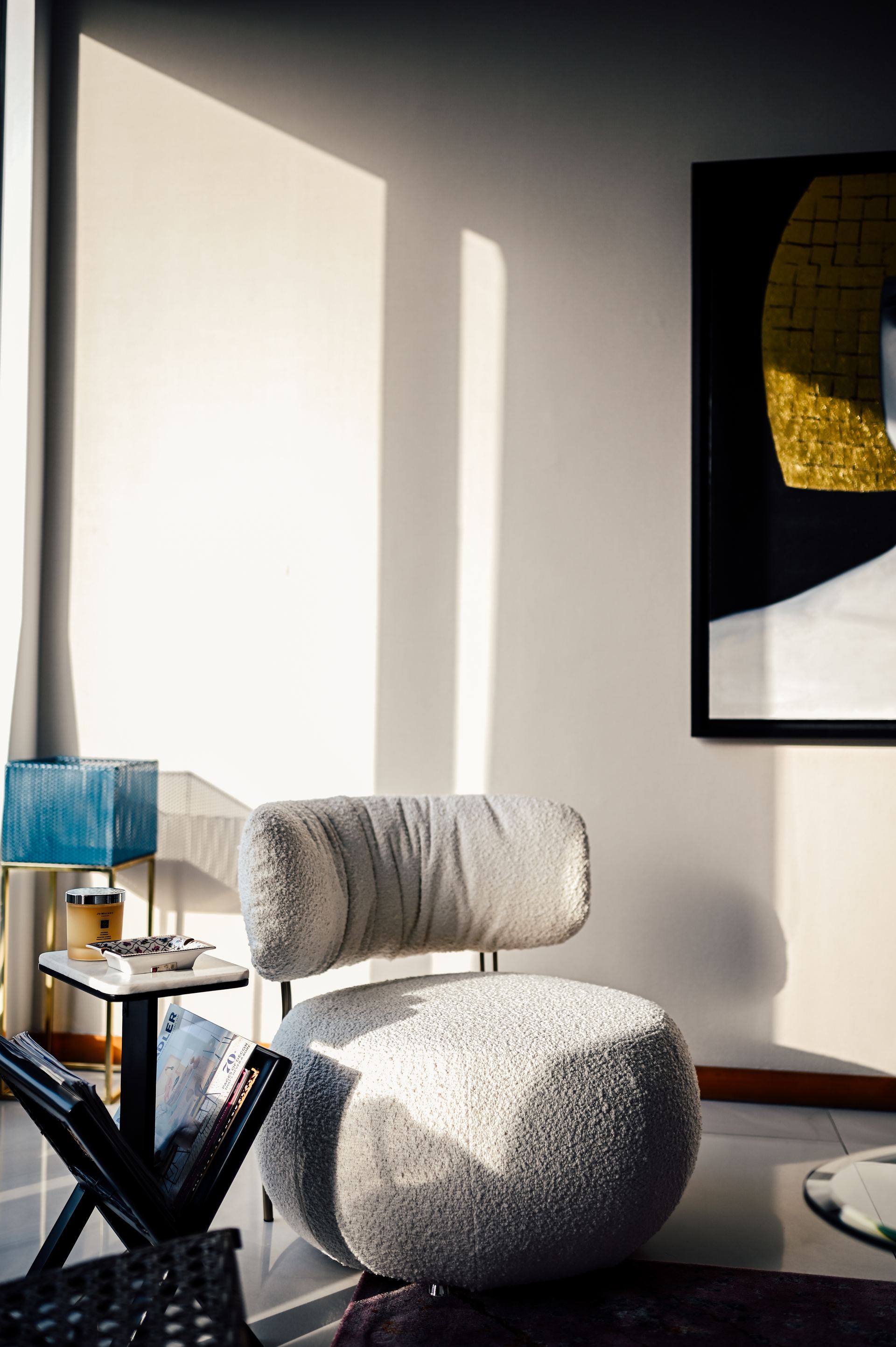 Bouclé lounge chair catching afternoon light beside a gold-framed abstract painting