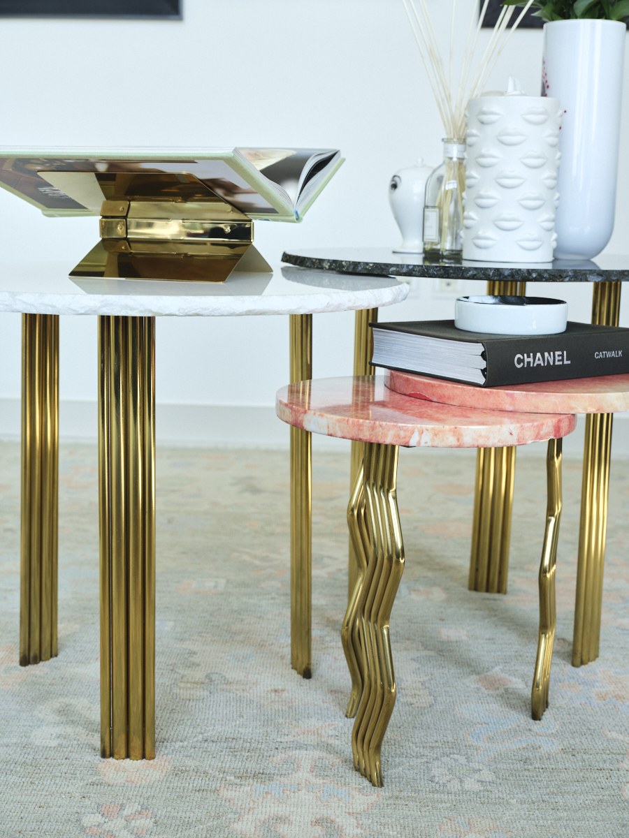 Nested gold-legged marble side tables styled with a lips-textured vase and a Chanel book