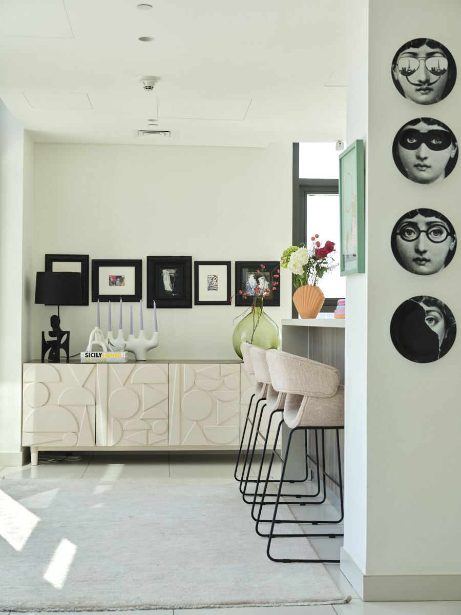 Fornasetti-style face plates beside a sideboard with candlesticks and framed art