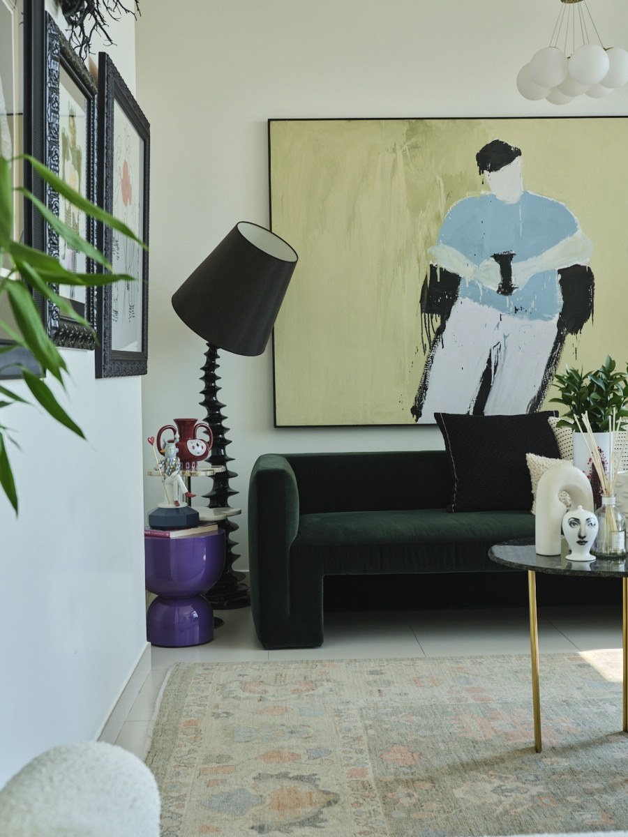 Green velvet sofa beneath a large figurative painting with a purple side table