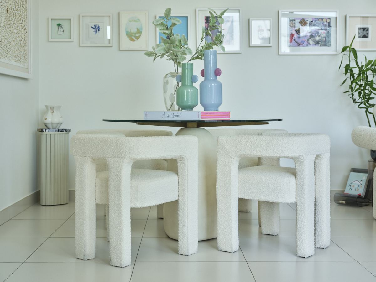 Bouclé dining stools around a round table topped with pastel glass vases