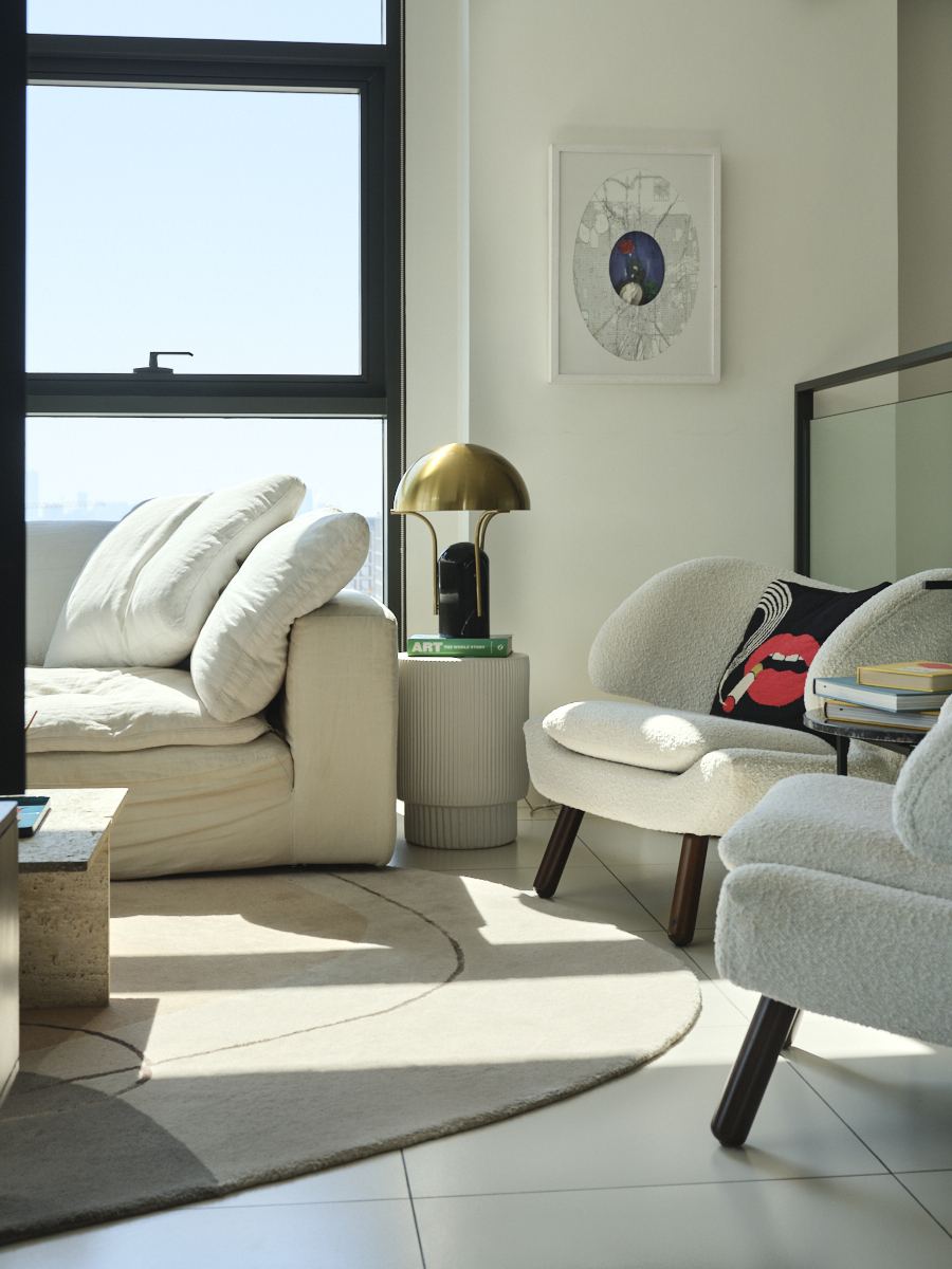 White bouclé armchairs beside a brass table lamp and gallery-style framed print