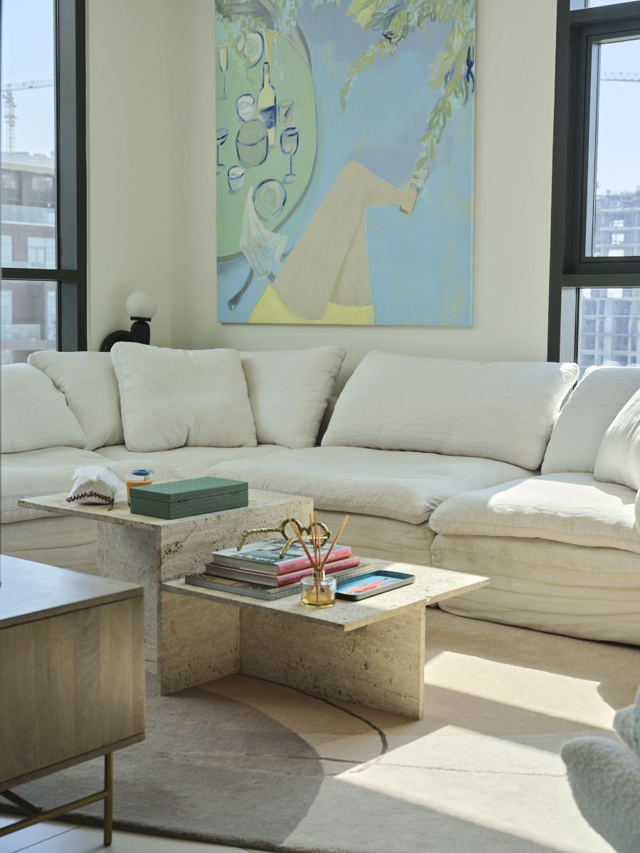 Cream sectional sofa beneath a pastel painting, with a travertine coffee table