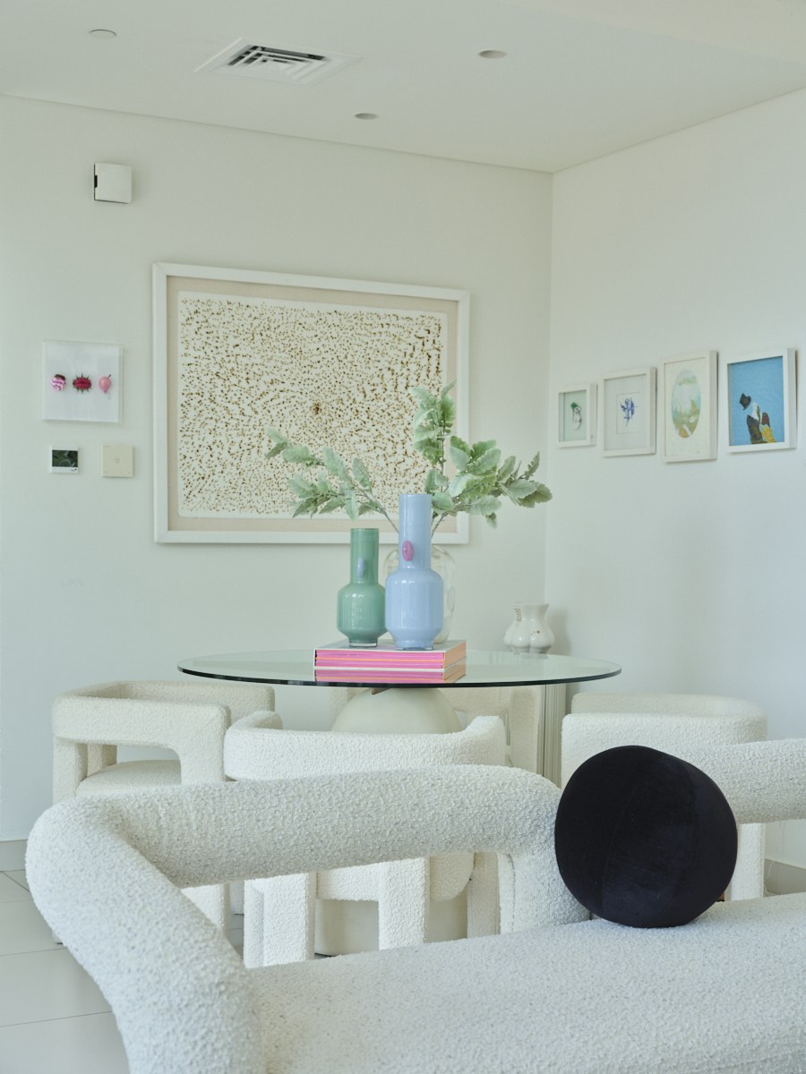 Round glass dining table with bouclé chairs beneath a gallery wall of framed art