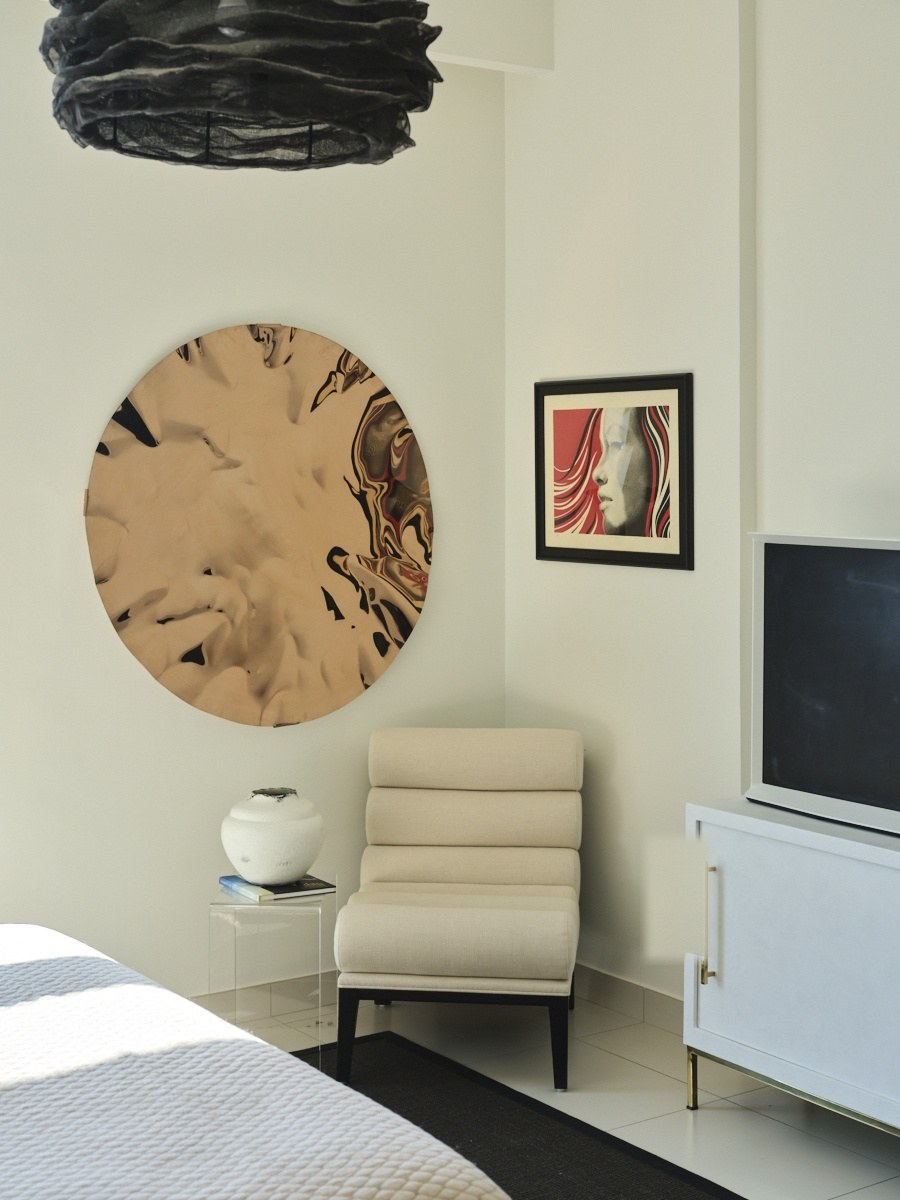 Round sculptural mirror and framed portrait above a bench at the foot of the bed