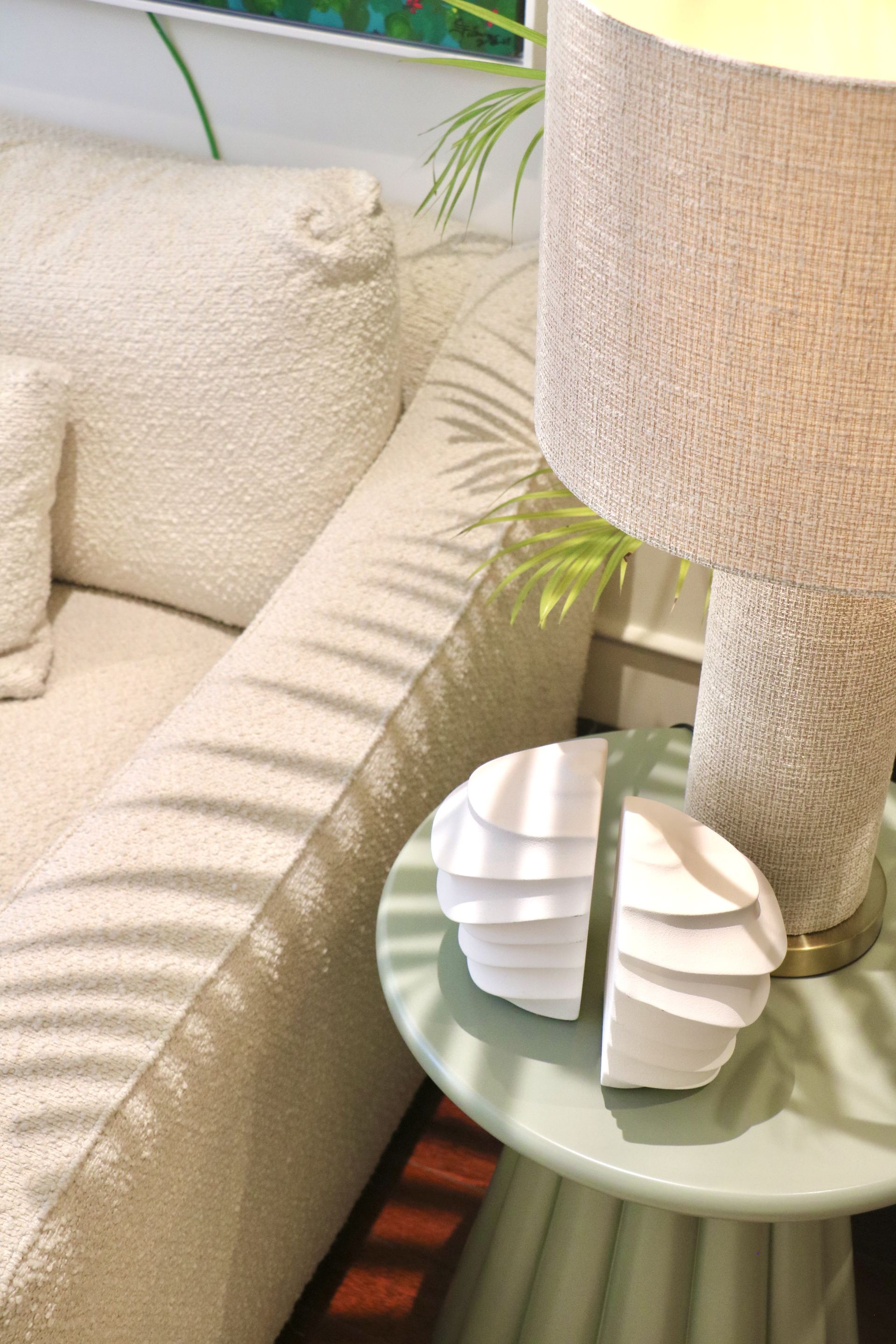 Fan-shaped ceramic bookends on a sage side table beside a bouclé sofa