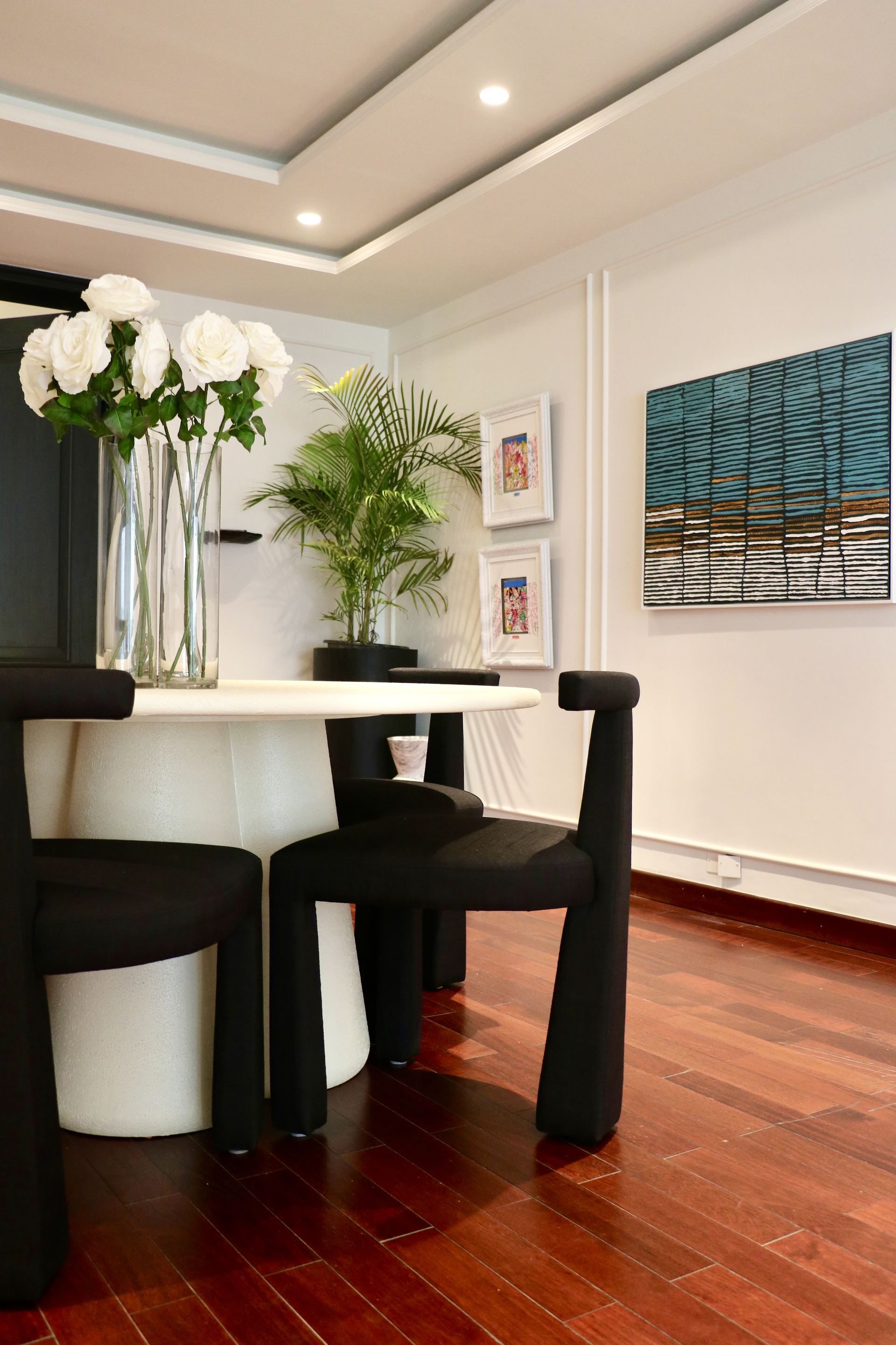Round marble dining table with black sculptural chairs beside framed art