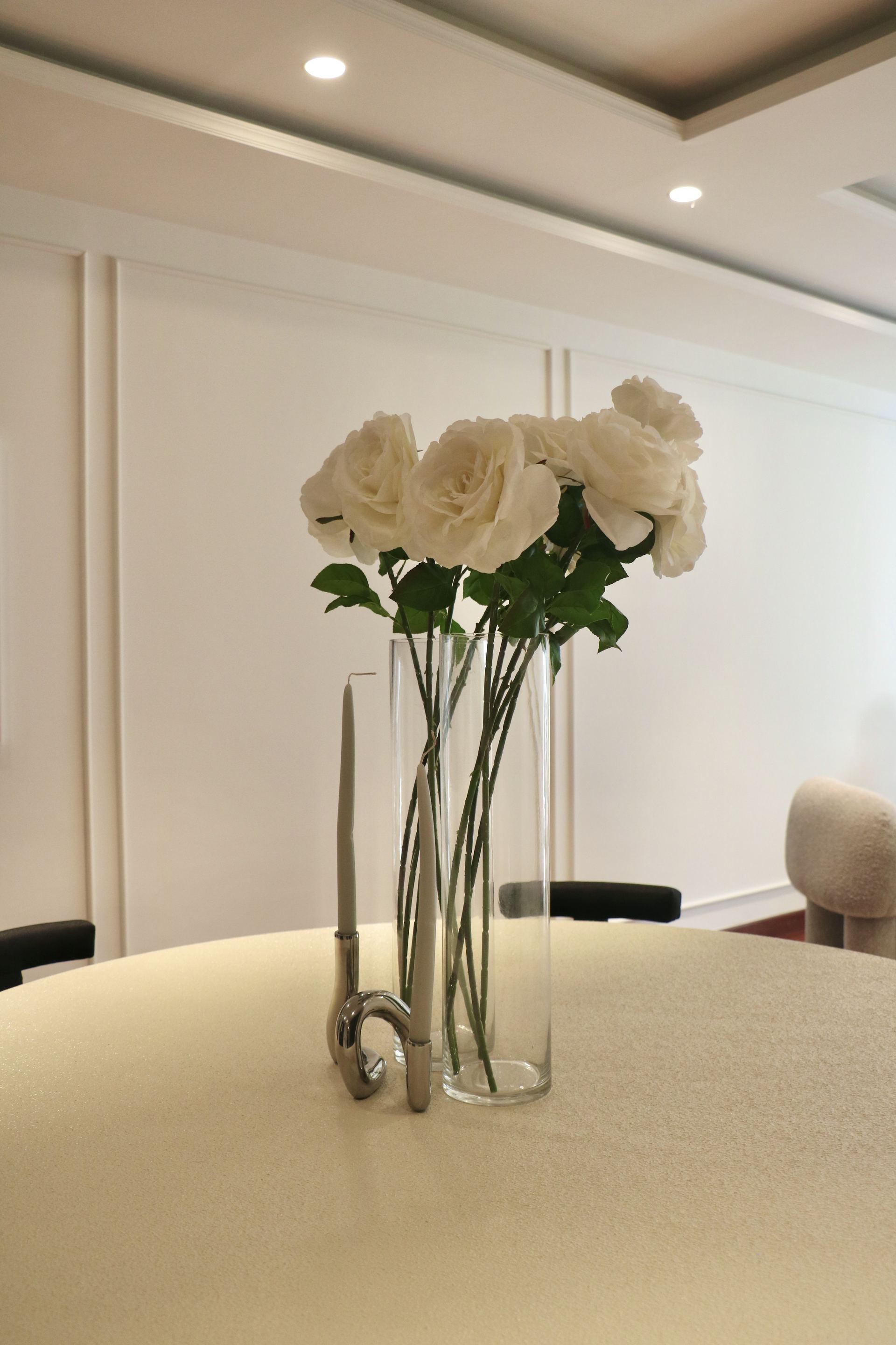 Glass vase of white roses with a silver candlestick on a cream dining table