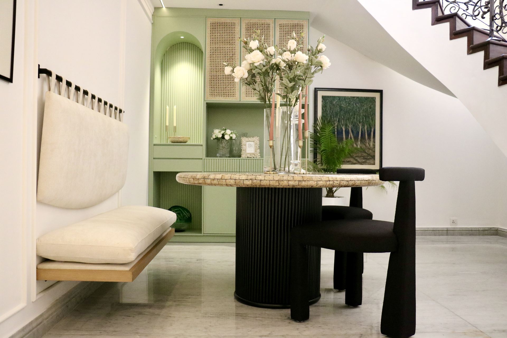 Wall-mounted bench and mosaic dining table beneath a curved wrought-iron staircase