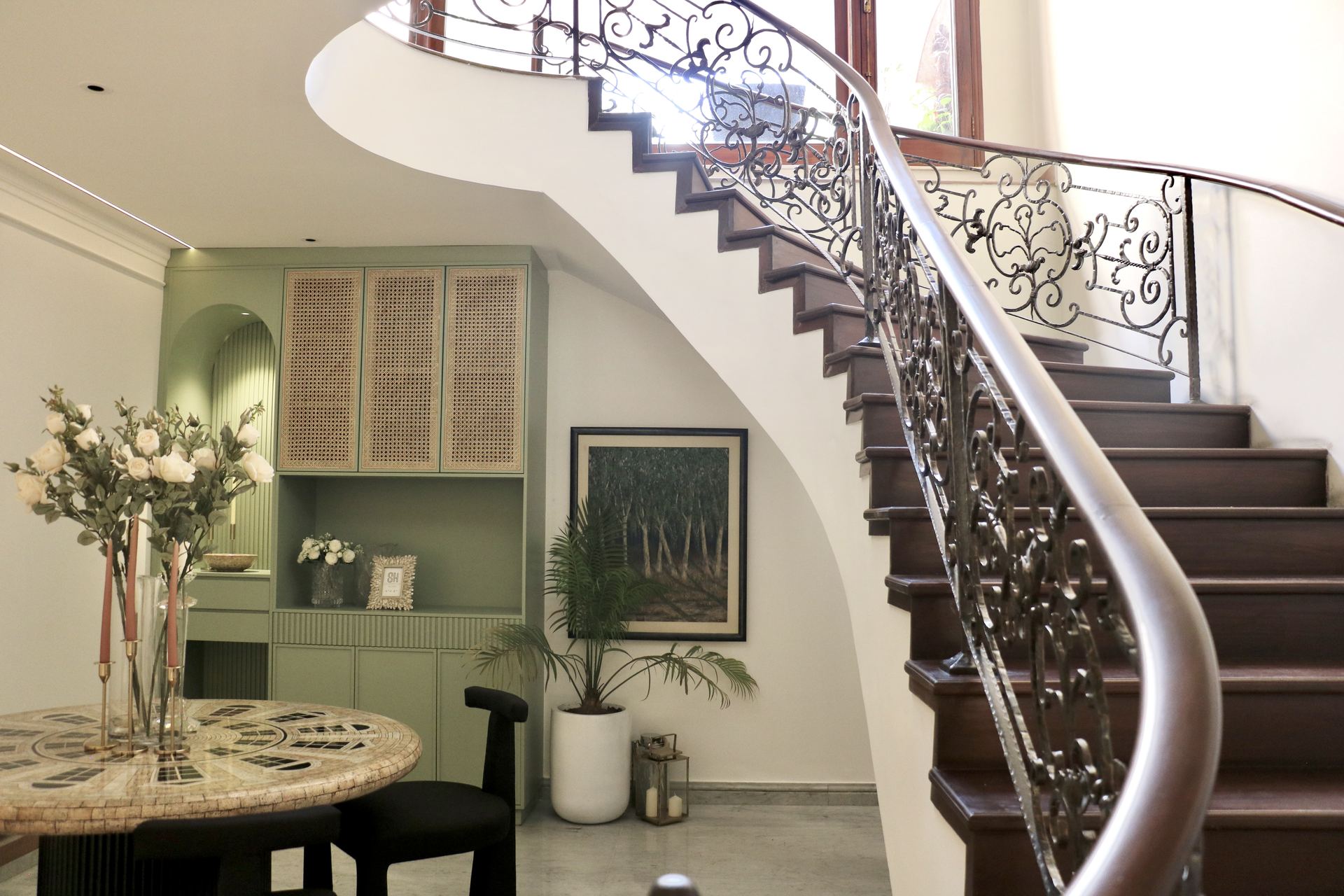 Wrought-iron spiral staircase beside a mosaic dining table and sage cabinetry