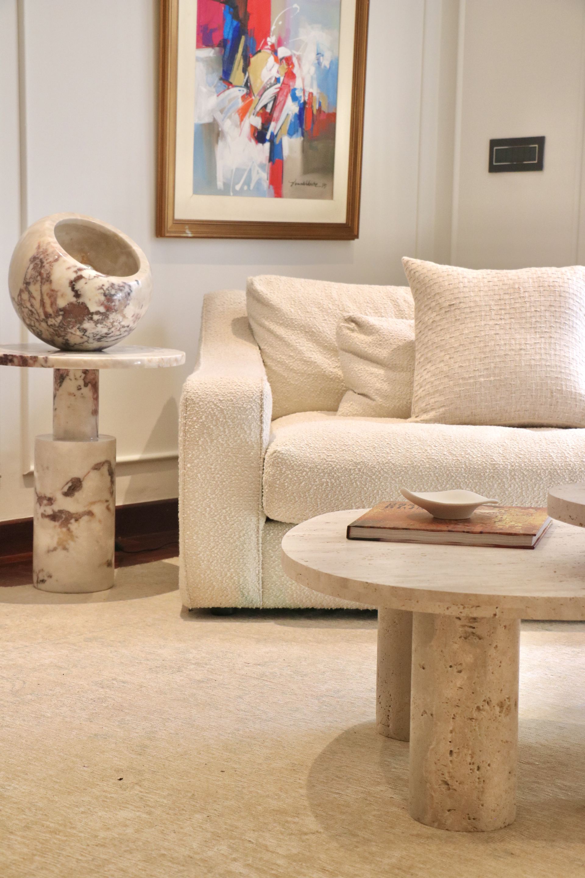 Round travertine side table with a stone bowl beside a bouclé sofa