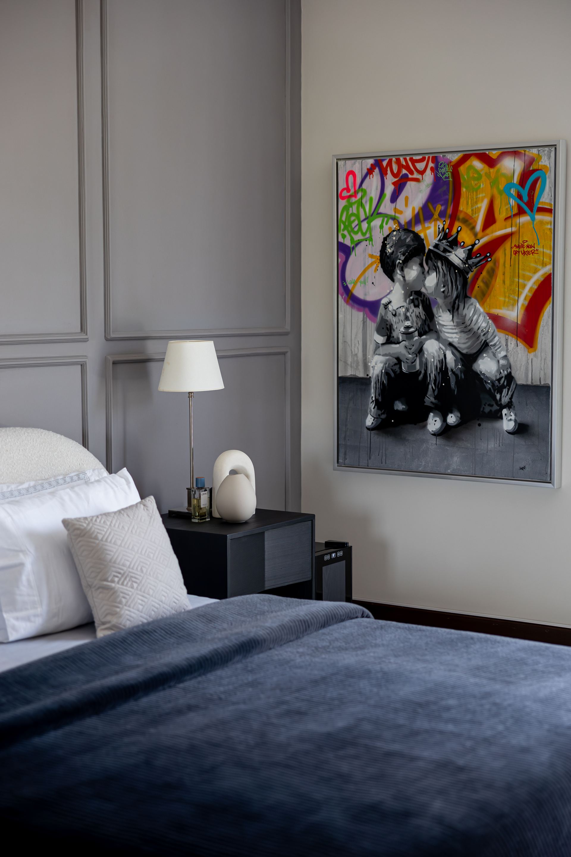 Graffiti-style portrait painting above a bedside table with a white ceramic lamp