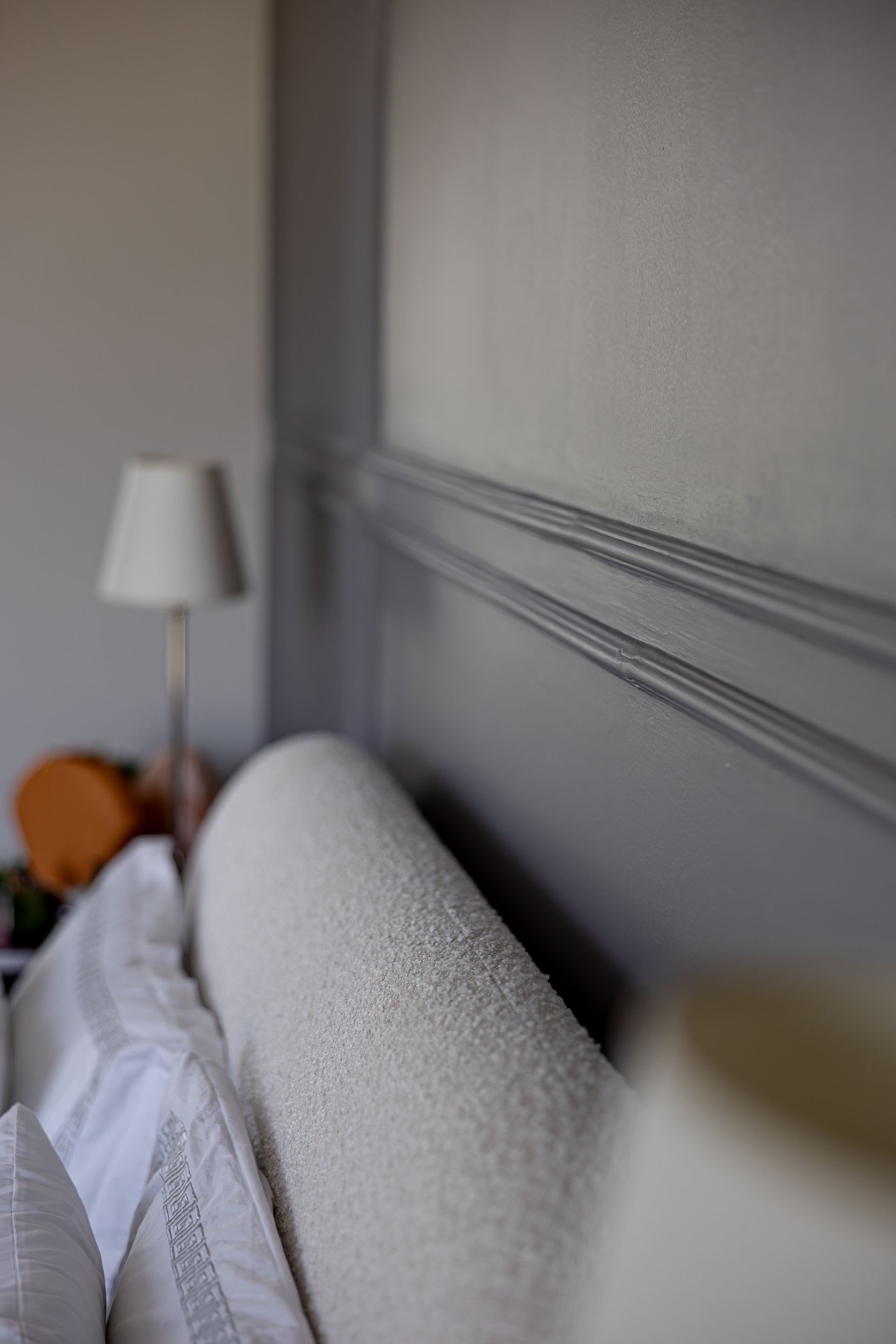 Close-up of a bouclé headboard against panelled grey wallpaper