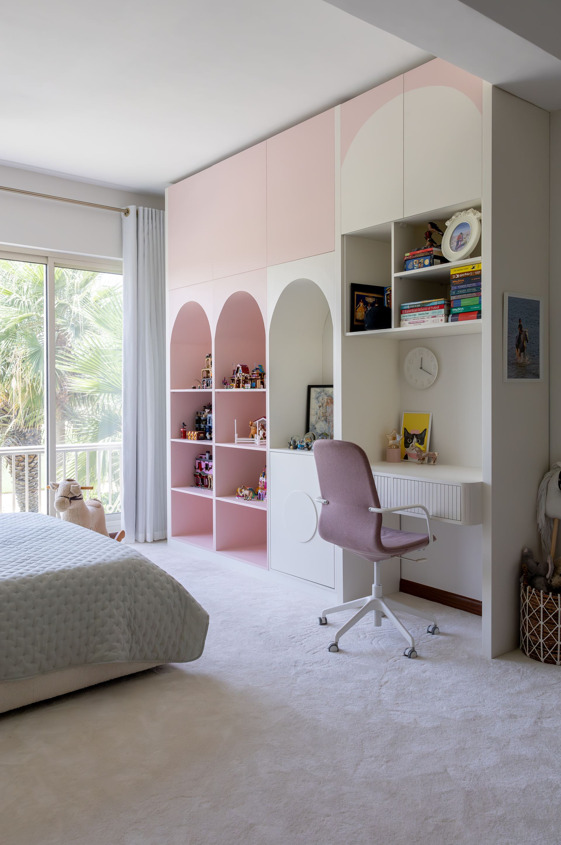 Pink arched shelving and a built-in desk in a child's bedroom