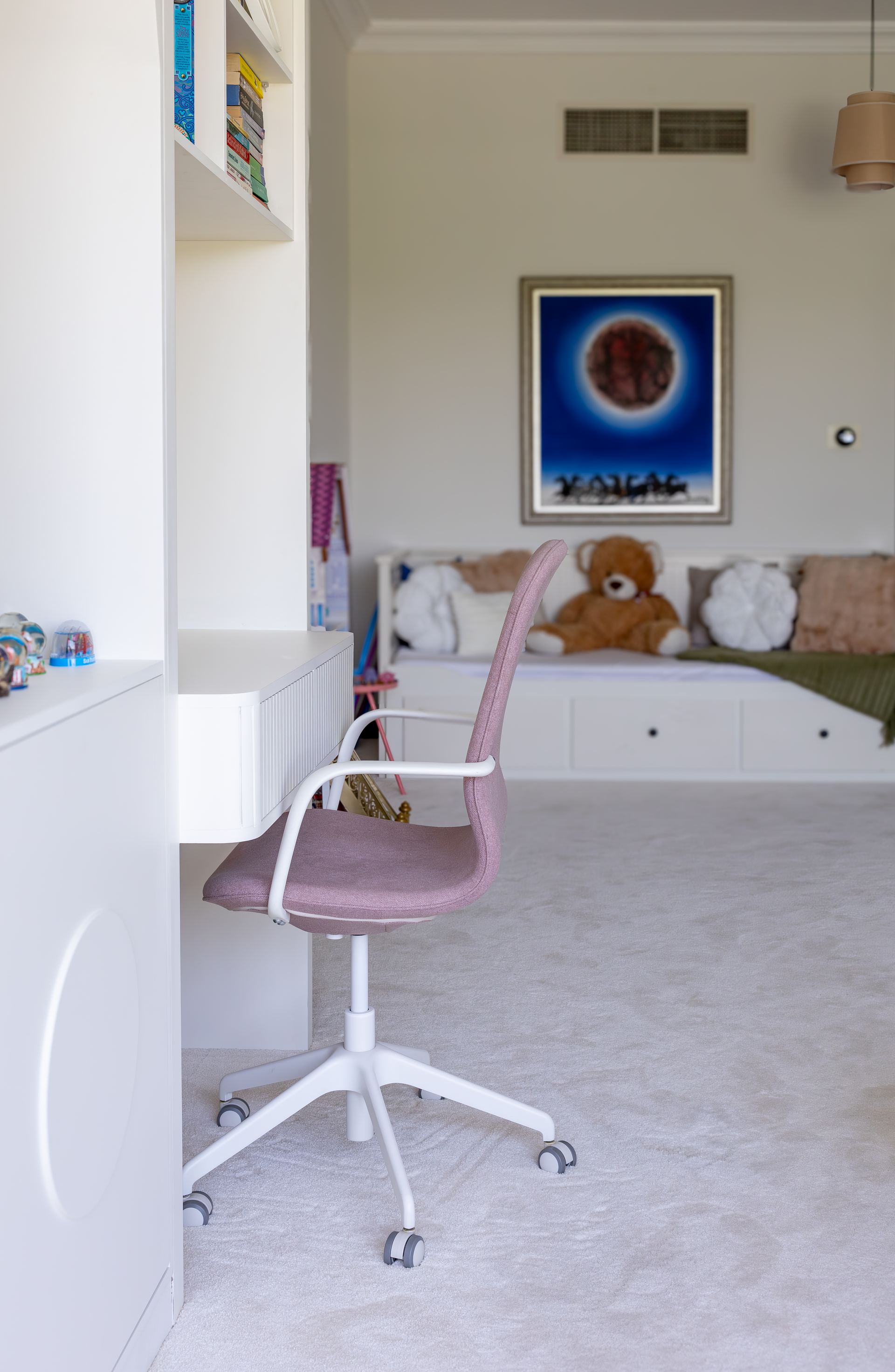 White desk with a pink task chair beside a built-in daybed with a teddy bear